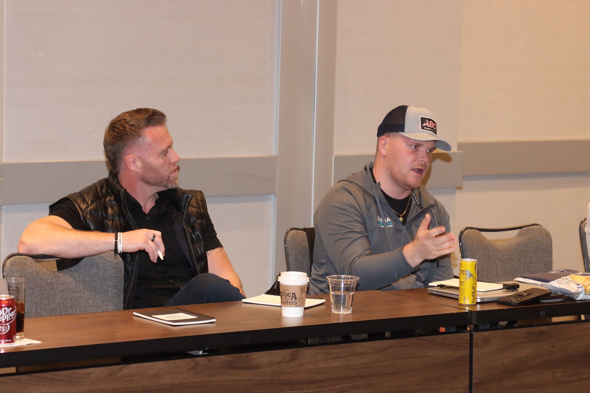 Two men at a table, one speaking and gesturing, the other listening attentively during a meeting.