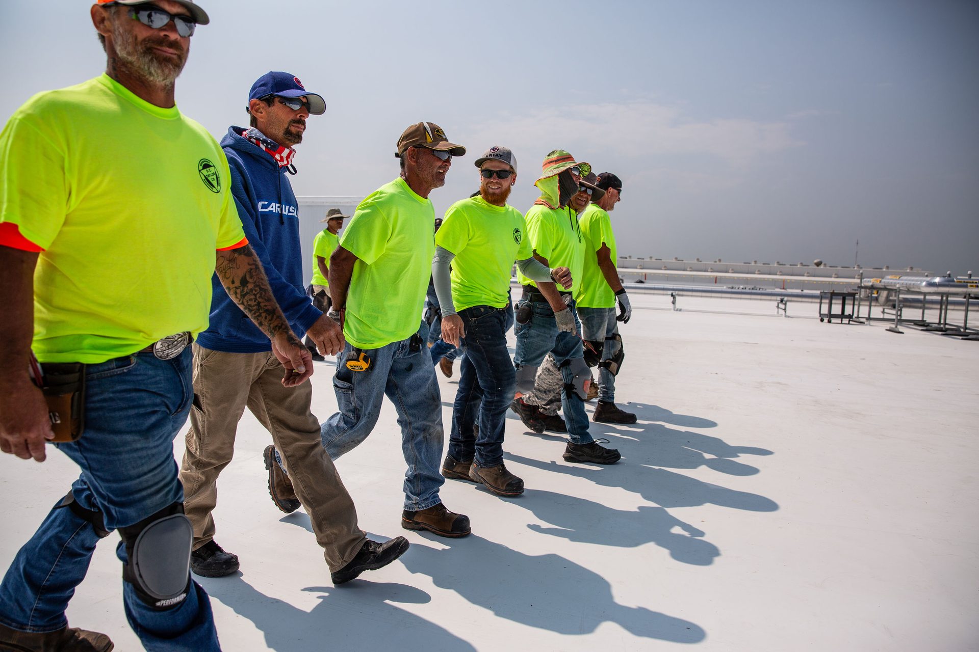 Group of men in bright yellow work shirts walking on a large white rooftop.