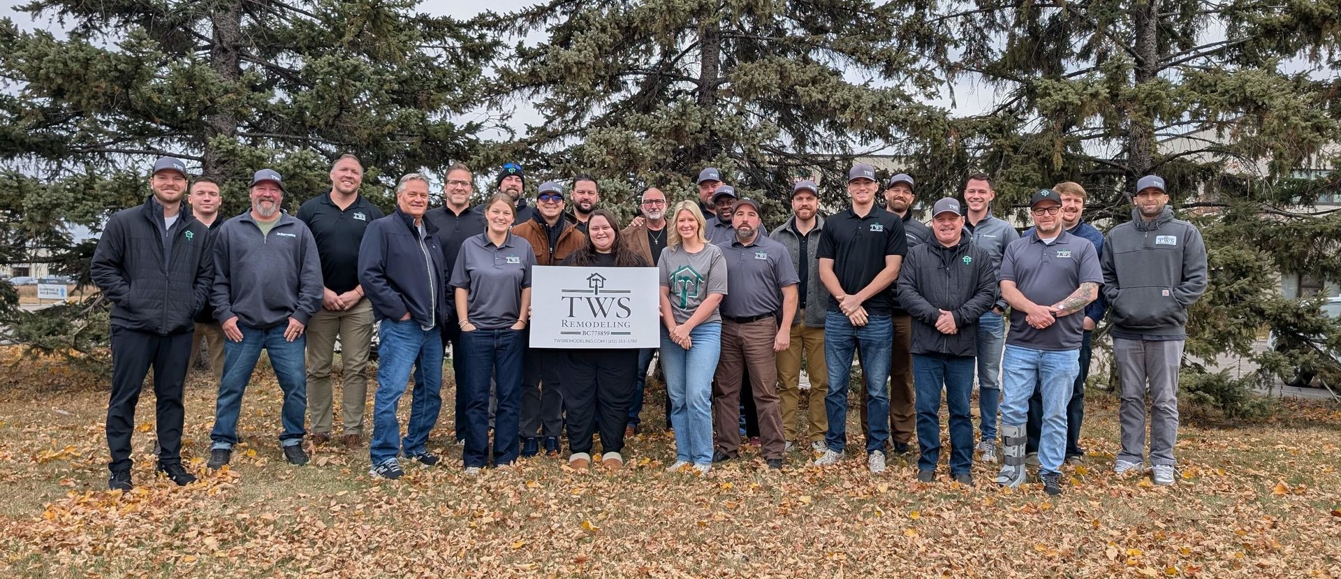 TWS Remodeling team, male and female, posing outdoors with their company sign in autumn.