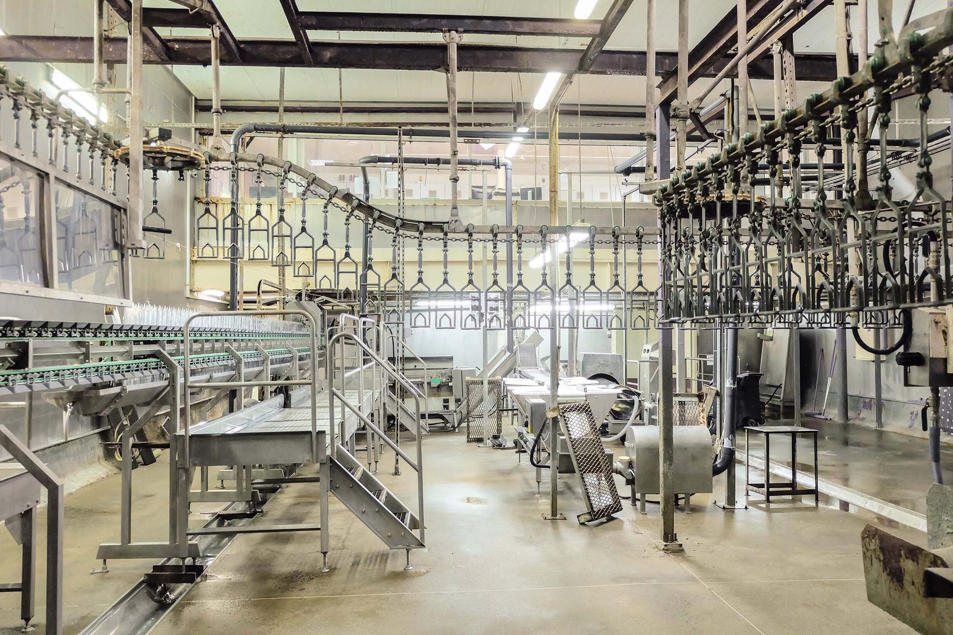 Empty poultry processing plant with stainless steel equipment, conveyors, and overhead hooks.