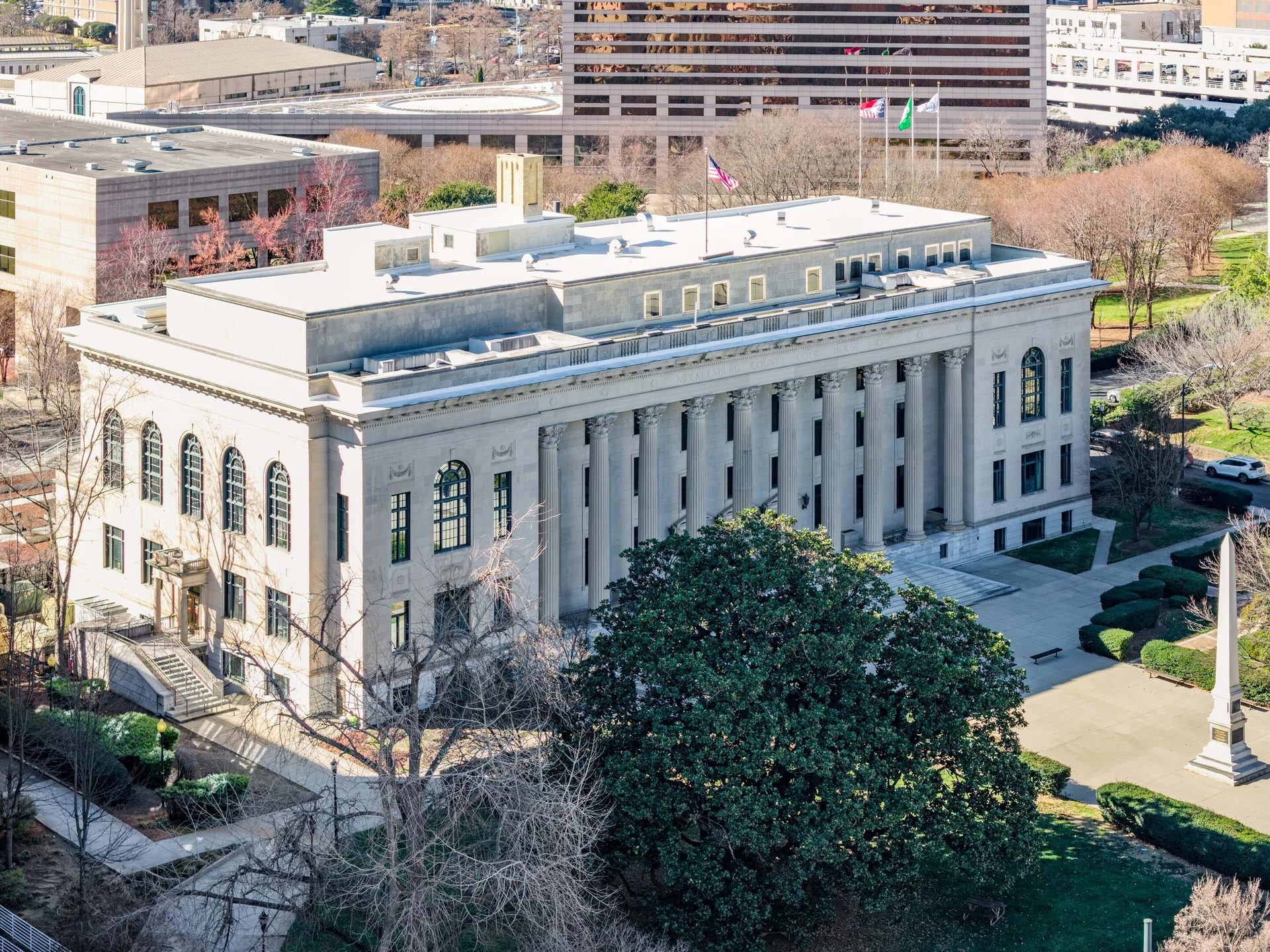 An aerial view of a grand classical courthouse building with columns and arched windows amidst trees and city.
