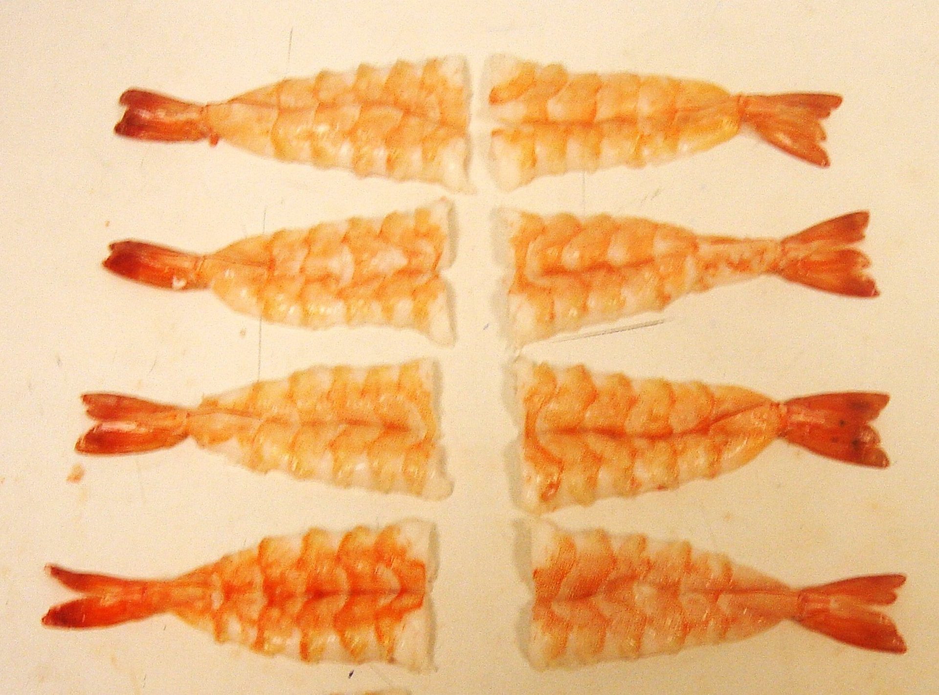 Eight cooked, peeled shrimp halves arranged in two rows on a white surface.