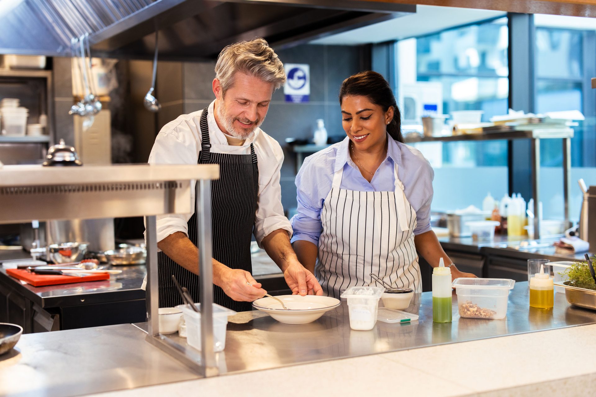 Two chefs, a man and a woman, collaborating in a professional kitchen, plating a dish.