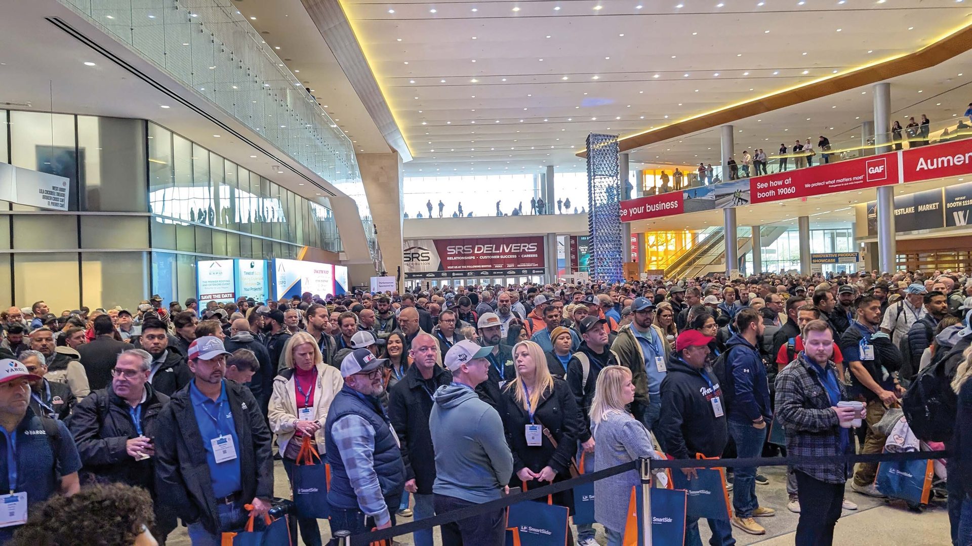 A large crowd of attendees fills a spacious convention hall at a trade show.