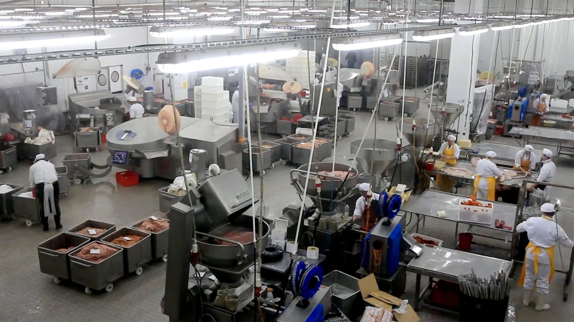 High-angle view of a meat processing plant with workers, industrial machinery, and processed meat.