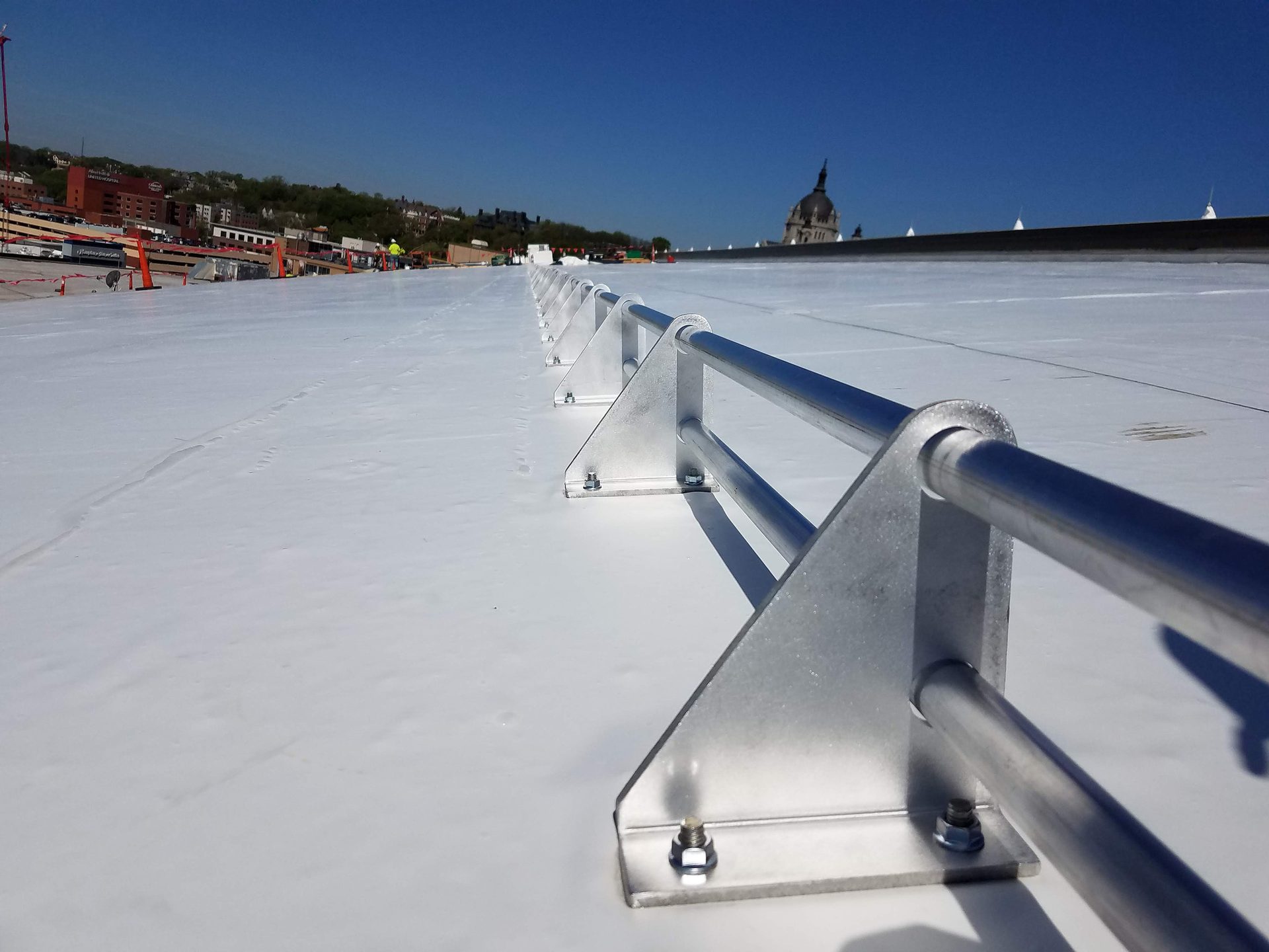 Rooftop safety railings on a white surface, with a city skyline and domed building in the distance.