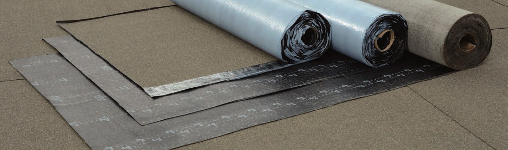 Rolls of roofing underlayment or waterproofing membrane, some unrolled on a surface.