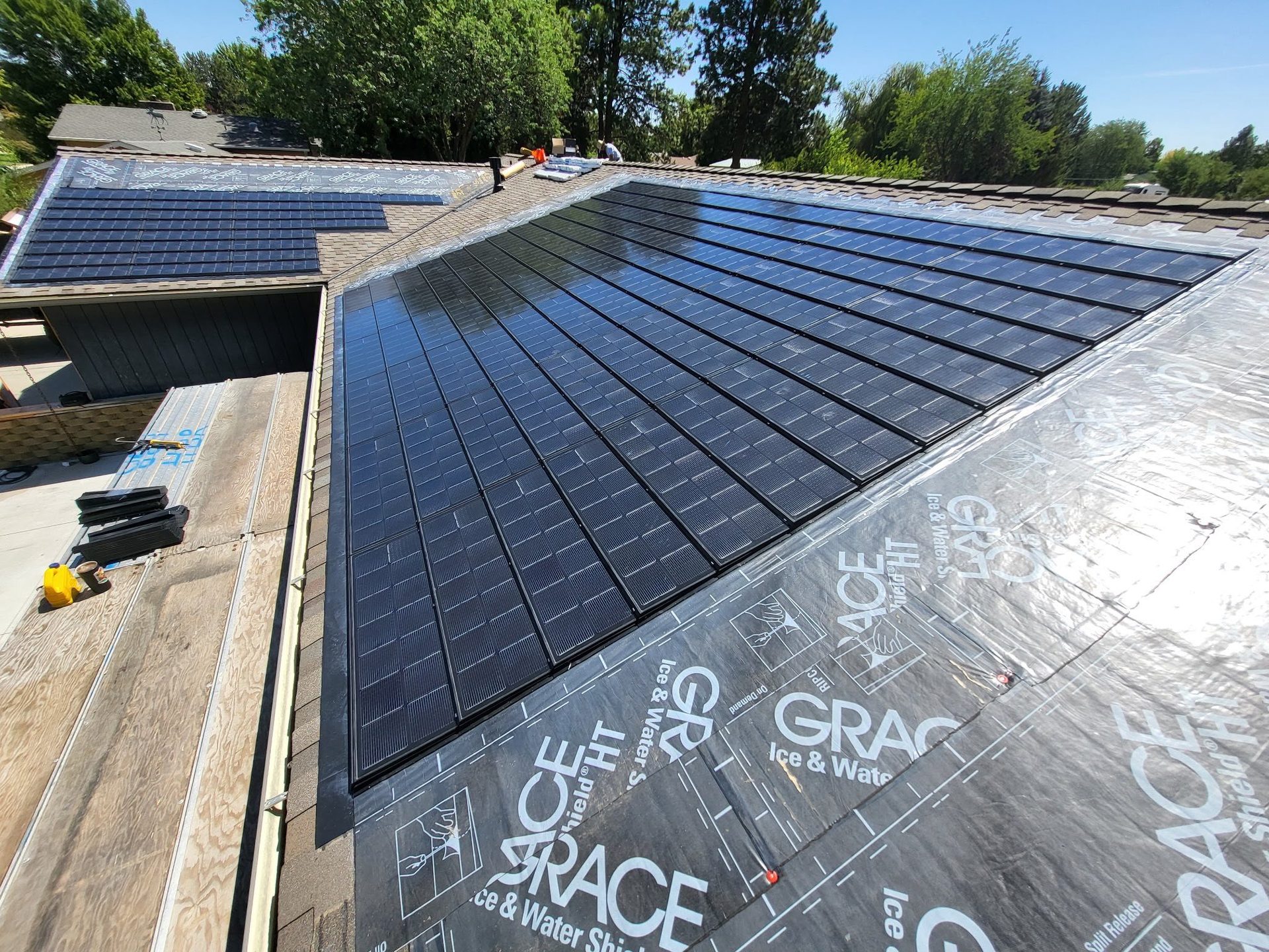 Solar roof tiles partially installed on a roof, next to visible Grace Ice & Water Shield underlayment.
