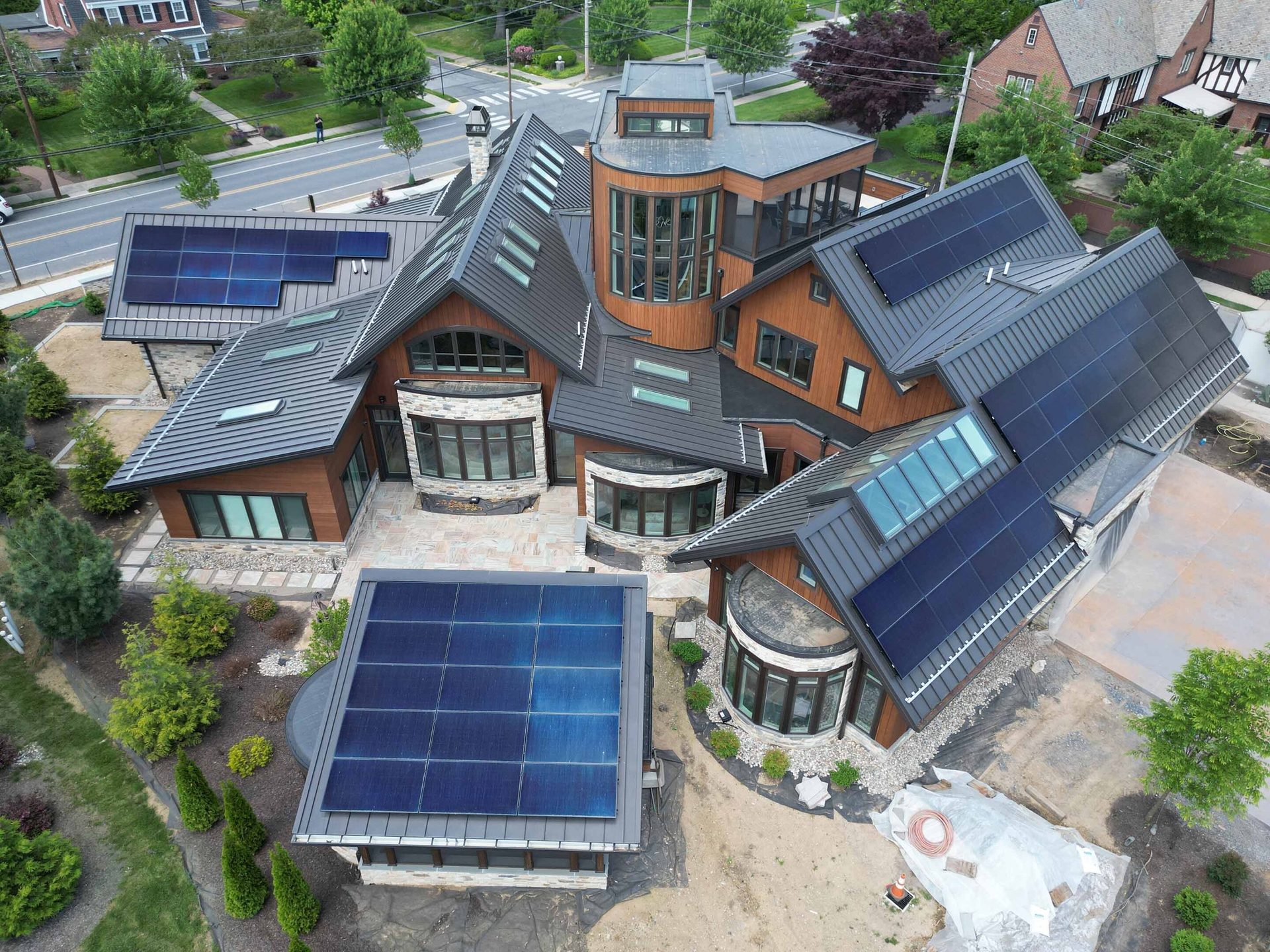 Aerial view of a large, modern house with multiple solar panel arrays on its metal roof.