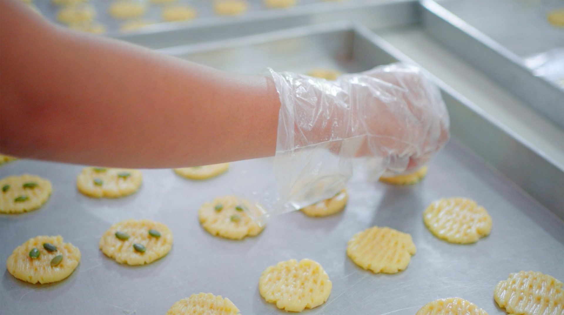 Gloved hand decorates cookies on a baking sheet, some with pumpkin seeds.