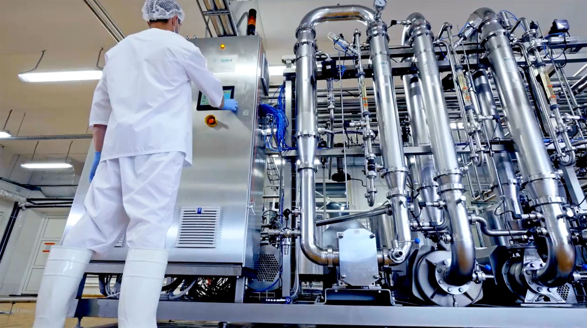 Worker in cleanroom attire operating a stainless steel industrial processing machine.