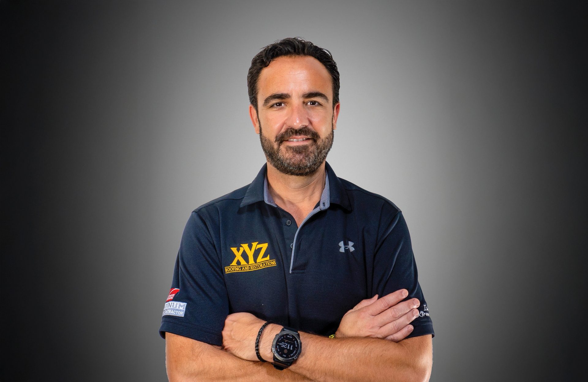 Man smiling with beard, dark polo shirt with "XYZ Roofing" logo, arms crossed.