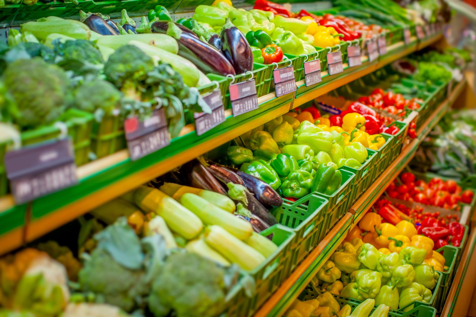 Colorful supermarket produce display with bell peppers, eggplants, zucchini, and broccoli.