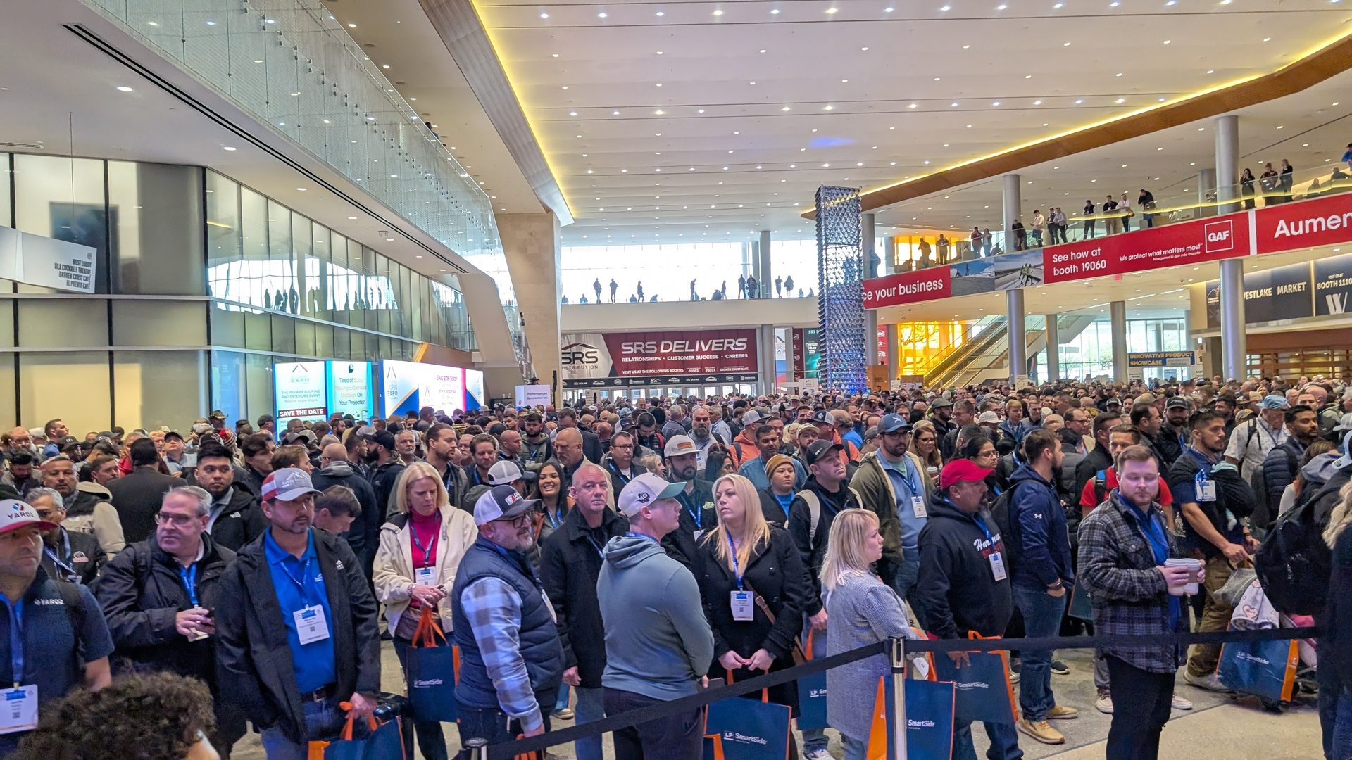 A massive crowd of people packed into a modern exhibition hall with overhead banners.