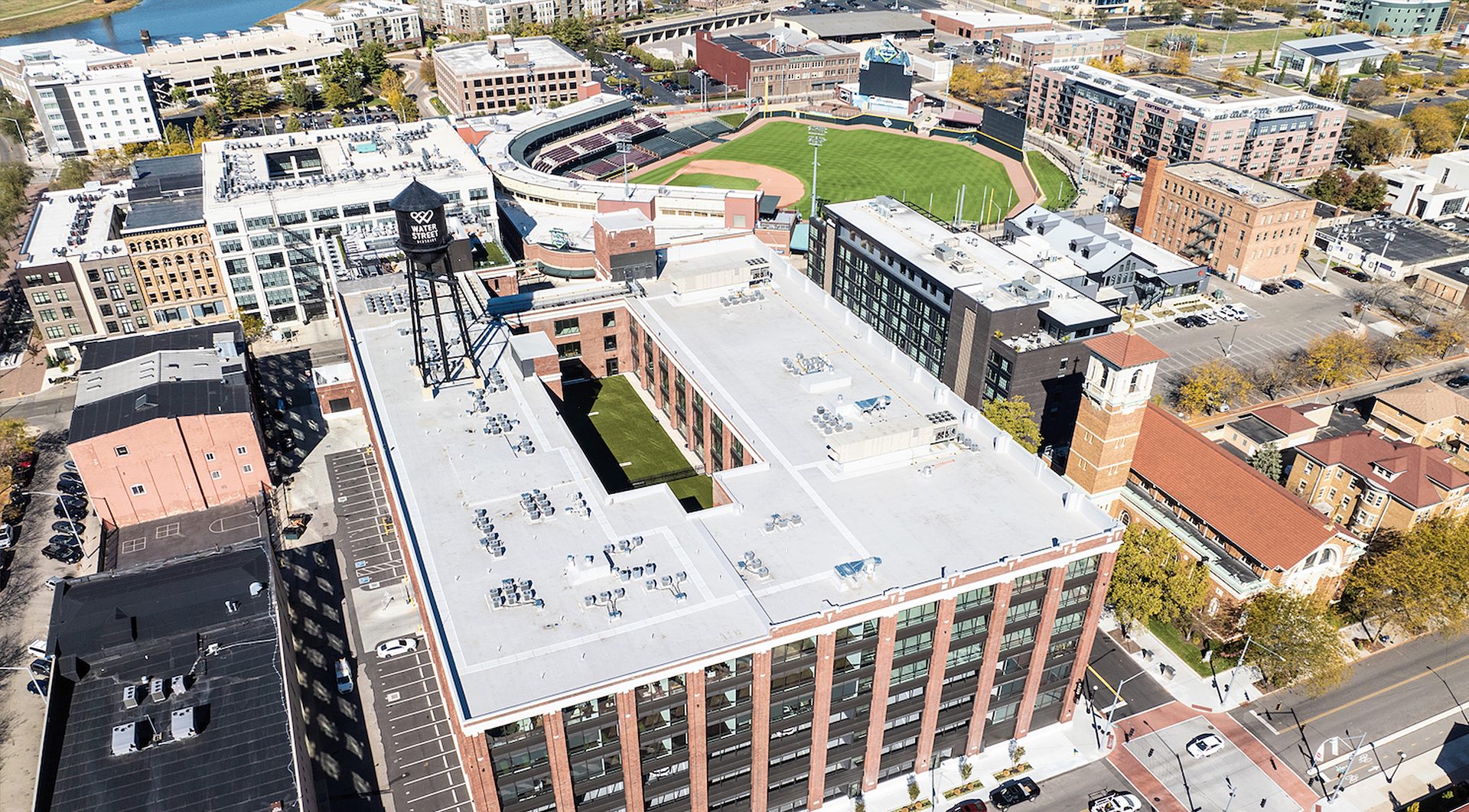 Aerial view of Water Street District: buildings, baseball stadium, river, and a large water tower.