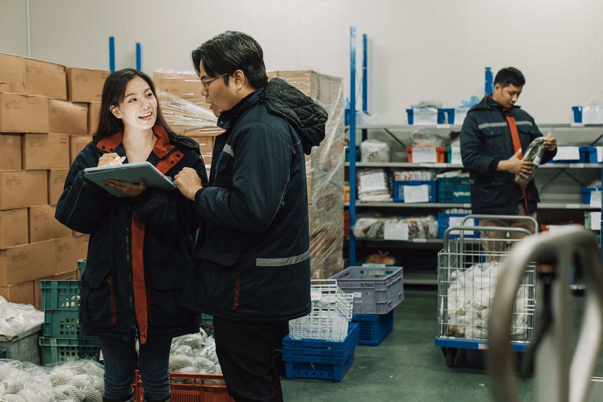 Warehouse workers collaborating with a tablet while another inspects goods in a cold storage facility.