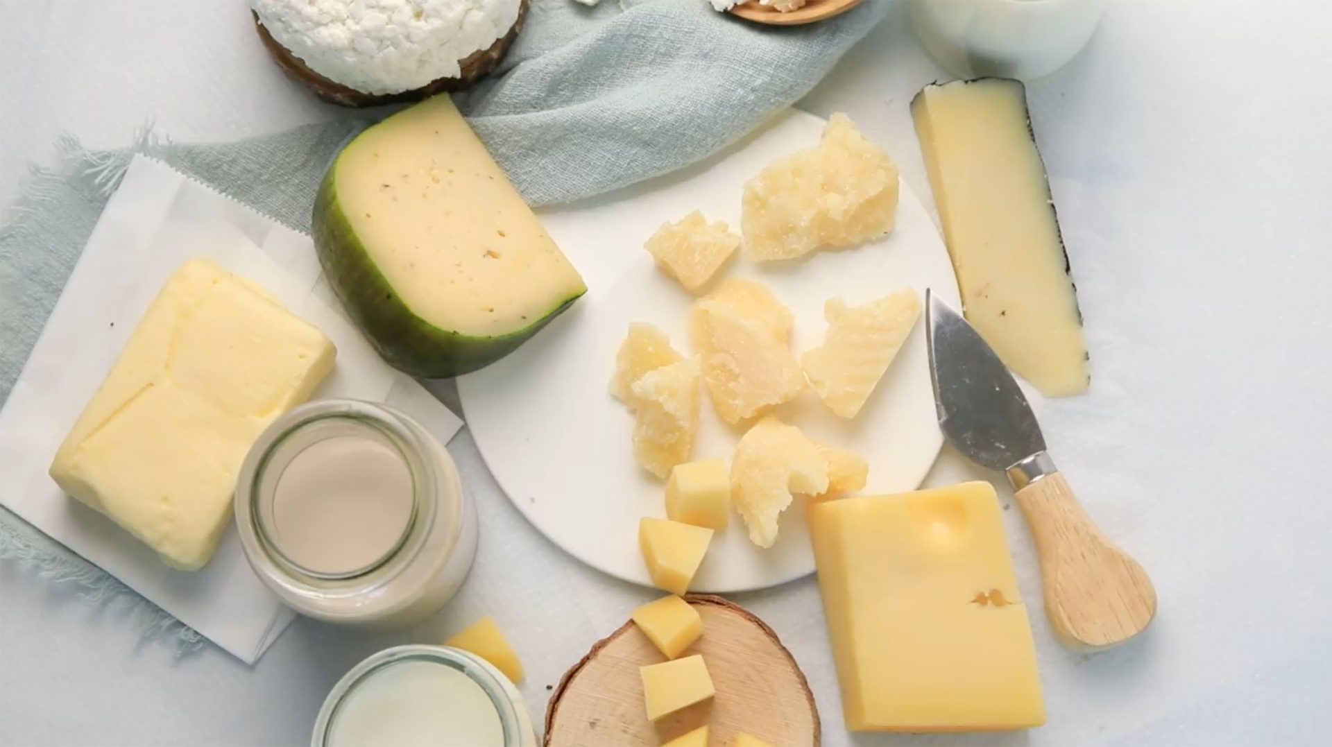 Assorted cheeses, milk, and a cheese knife on a light surface.