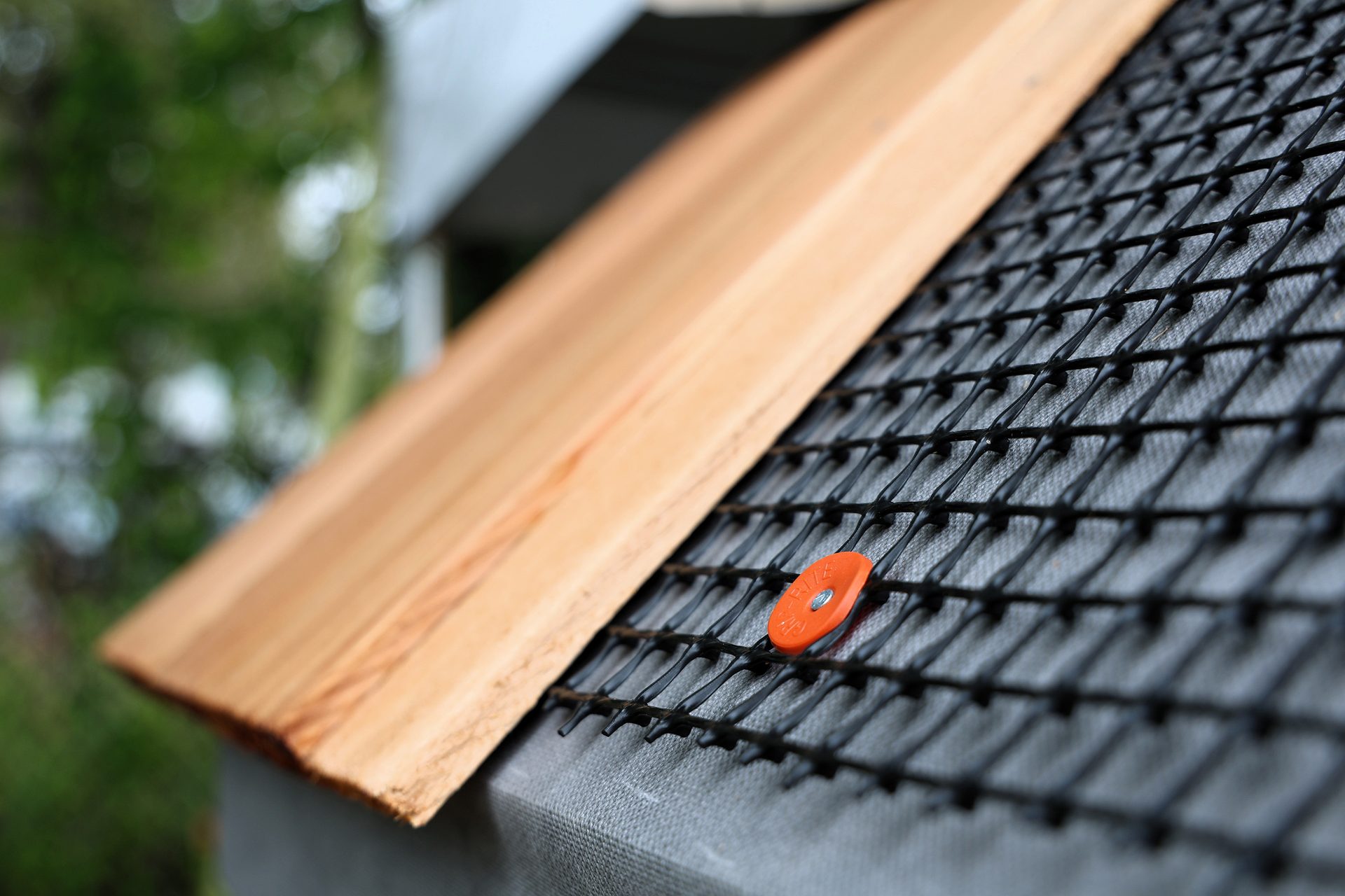Wooden shingle, black mesh, and orange fastener on a gray surface.