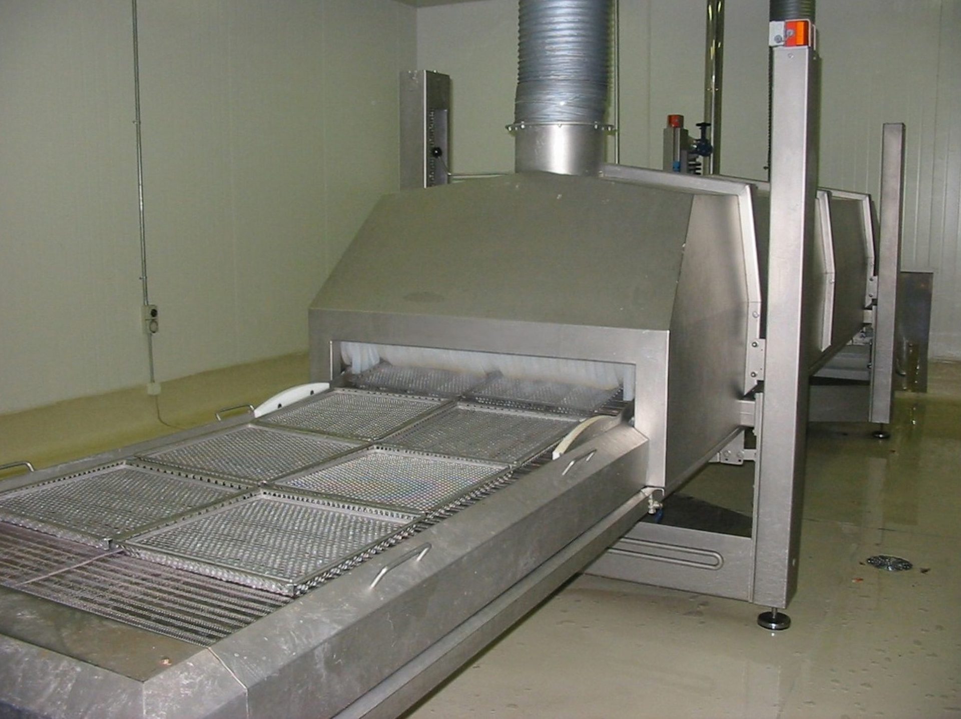 Stainless steel industrial processing machine with conveyor belt and metal trays in a clean room.