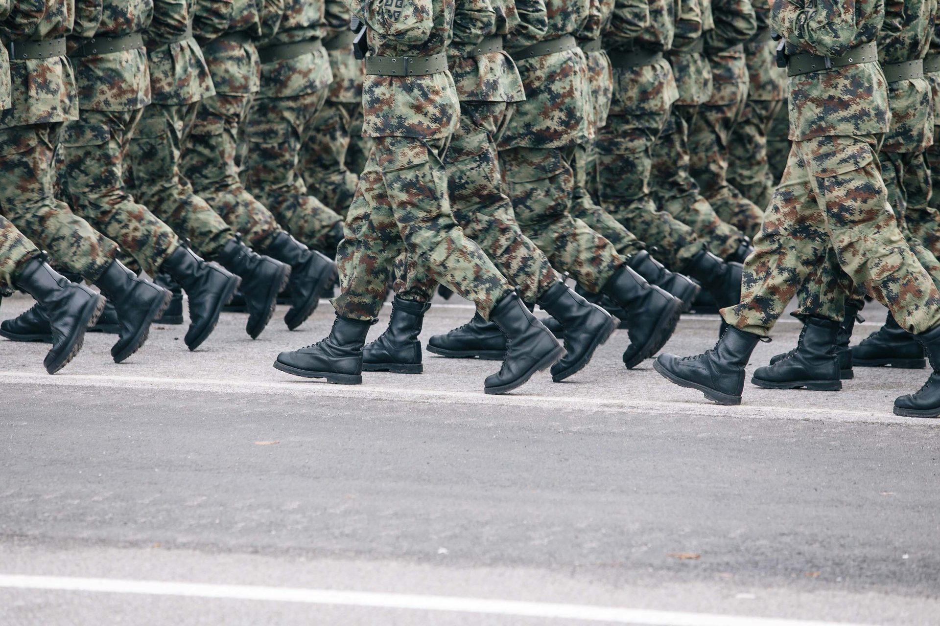 Soldiers in camouflage uniforms and black boots marching on a paved road.