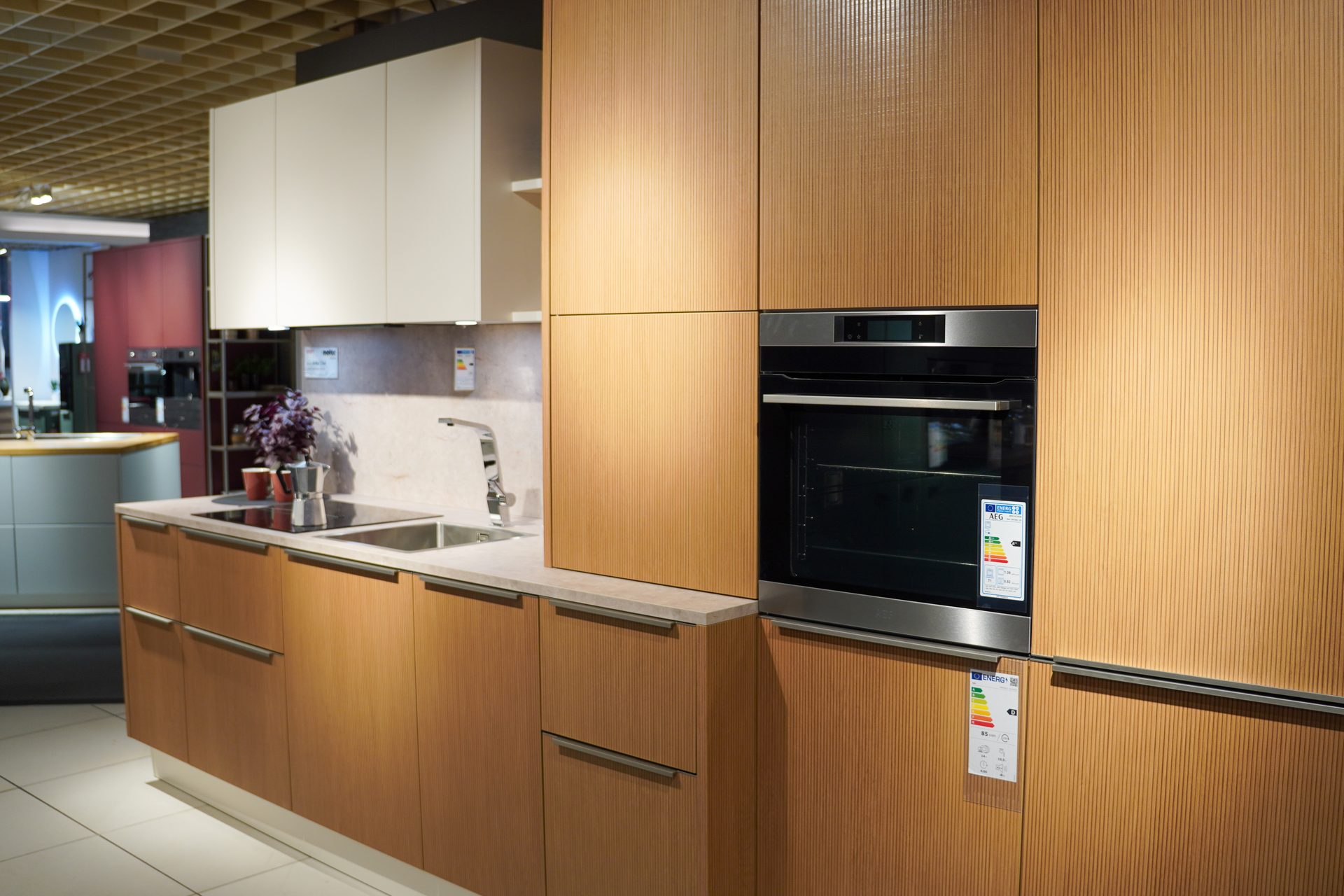 Modern kitchen with light wood cabinets, white upper units, stainless steel oven, sink, and cooktop.