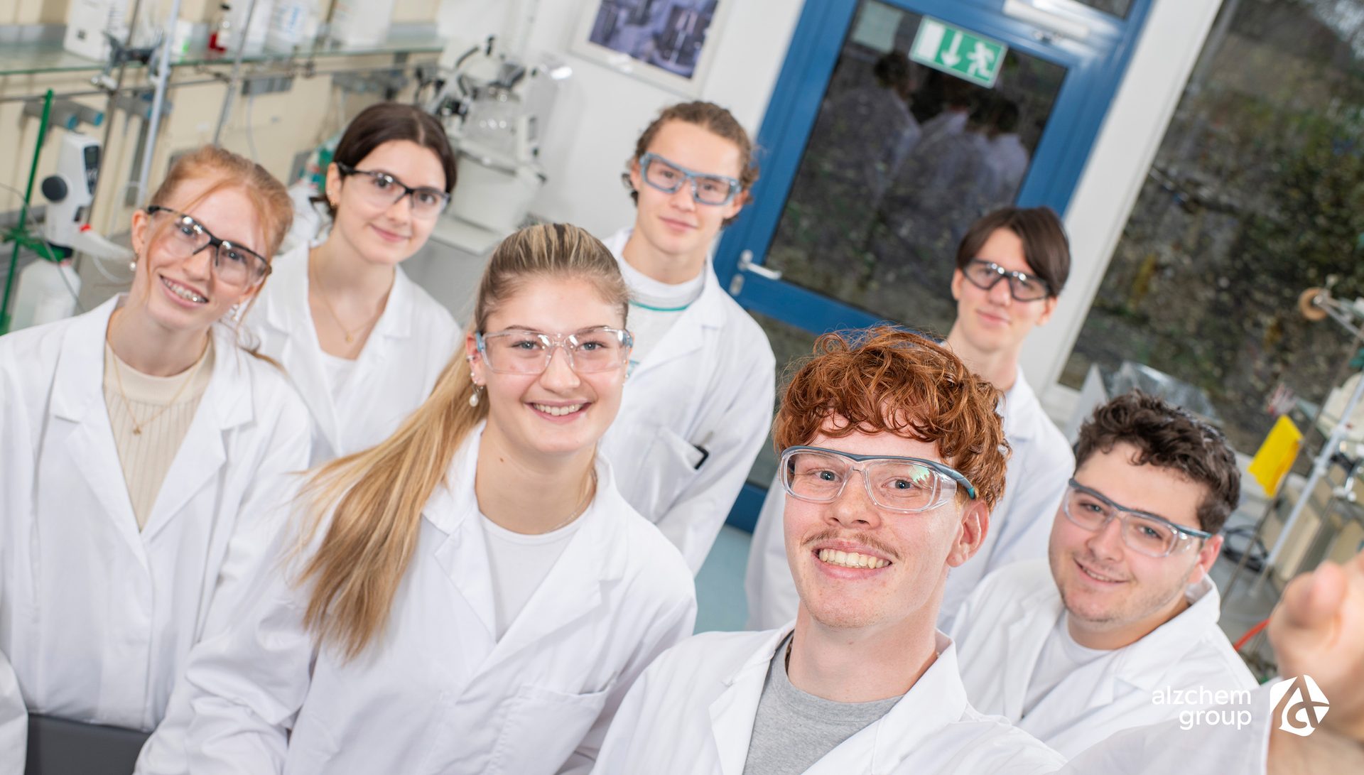Smiling group of students in lab coats and safety glasses in a lab.