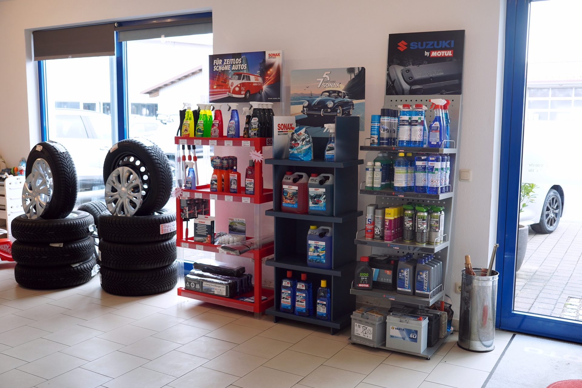 Car service center interior with stacks of tires, shelves displaying car care products, oils, and batteries.
