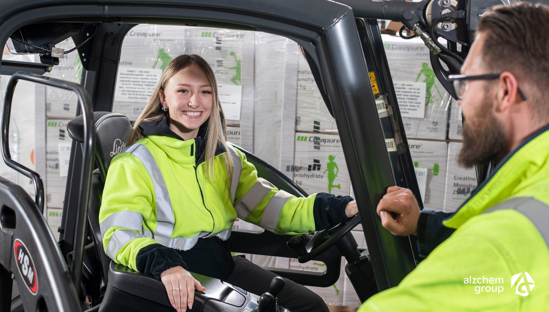 Smiling woman in forklift talking to man in warehouse.