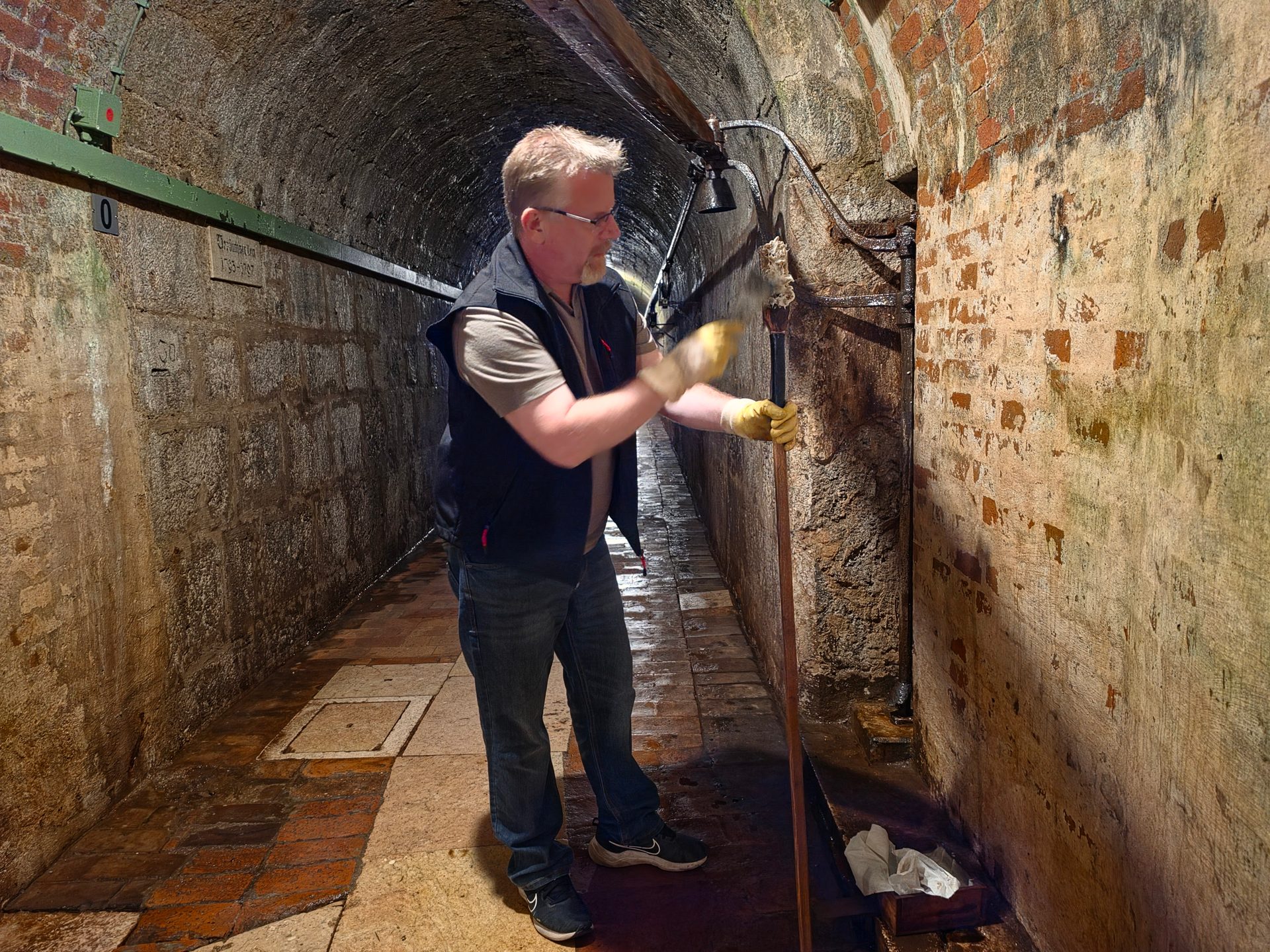 Man in a tunnel cleaning the wall with a long-handled tool.