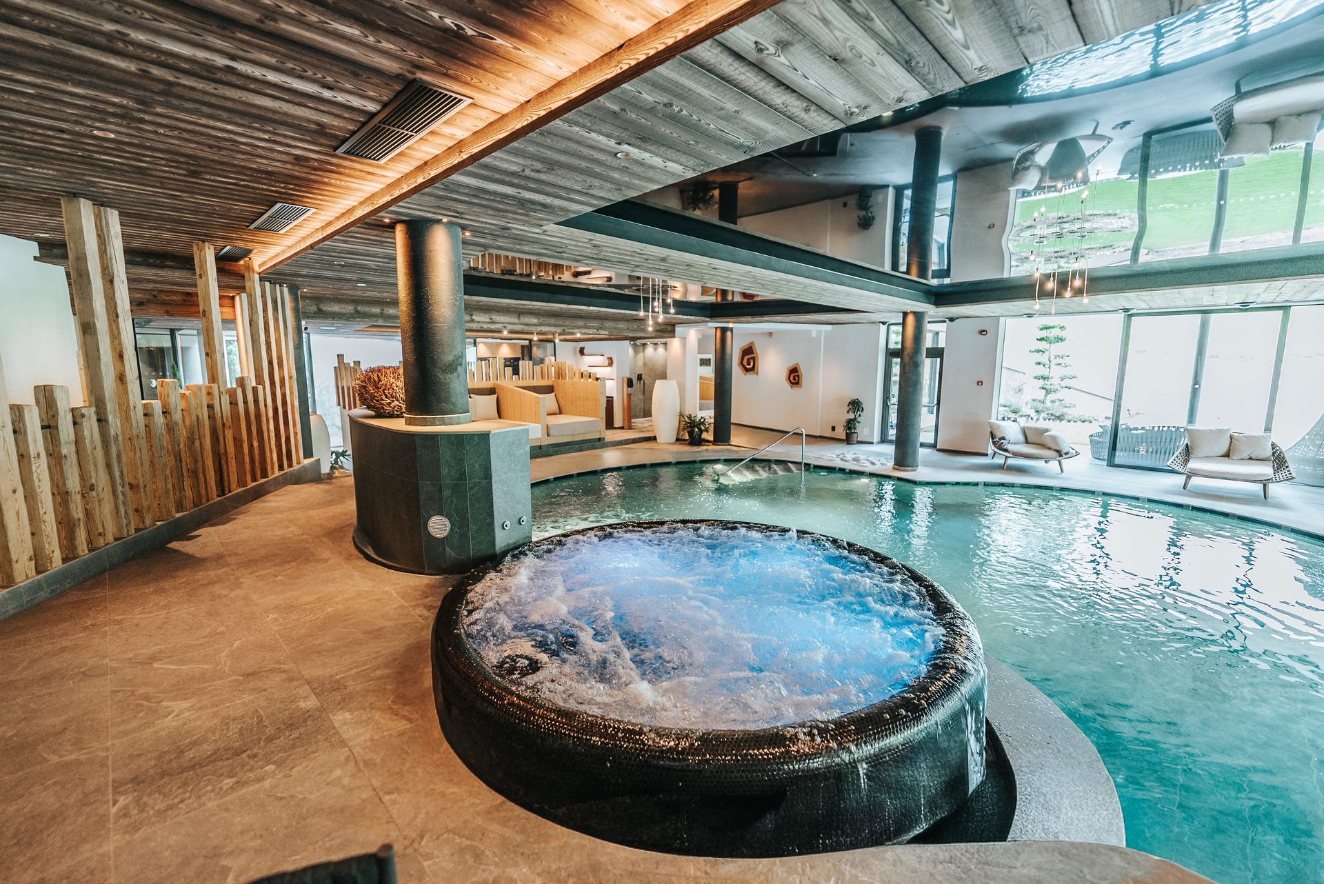 A luxurious indoor spa area featuring a bubbling hot tub, large swimming pool, and stylish wood decor.