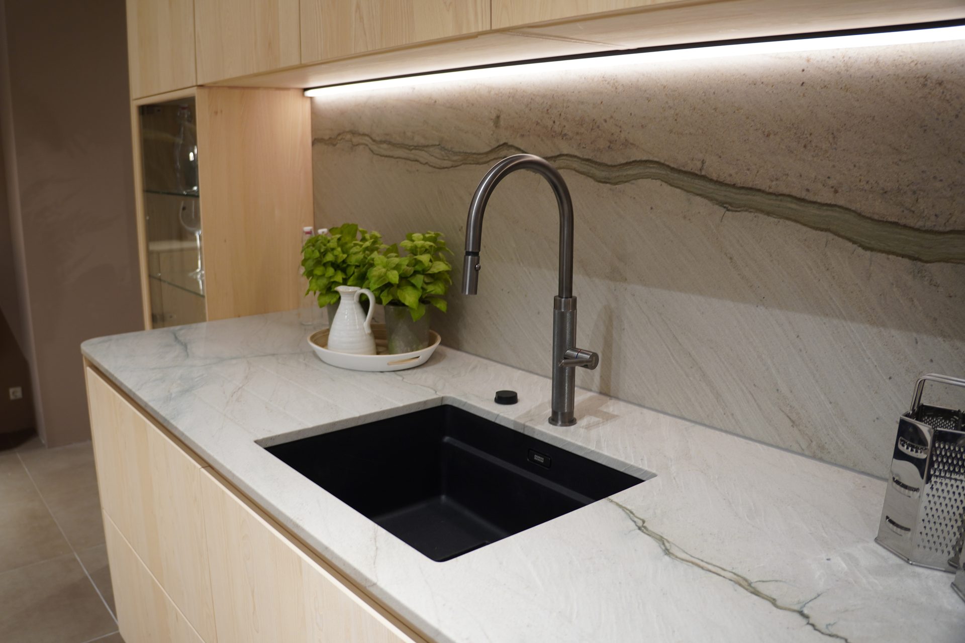 Modern kitchen featuring a black sink, sleek faucet, light marble countertop, and a striking natural stone backsplash.