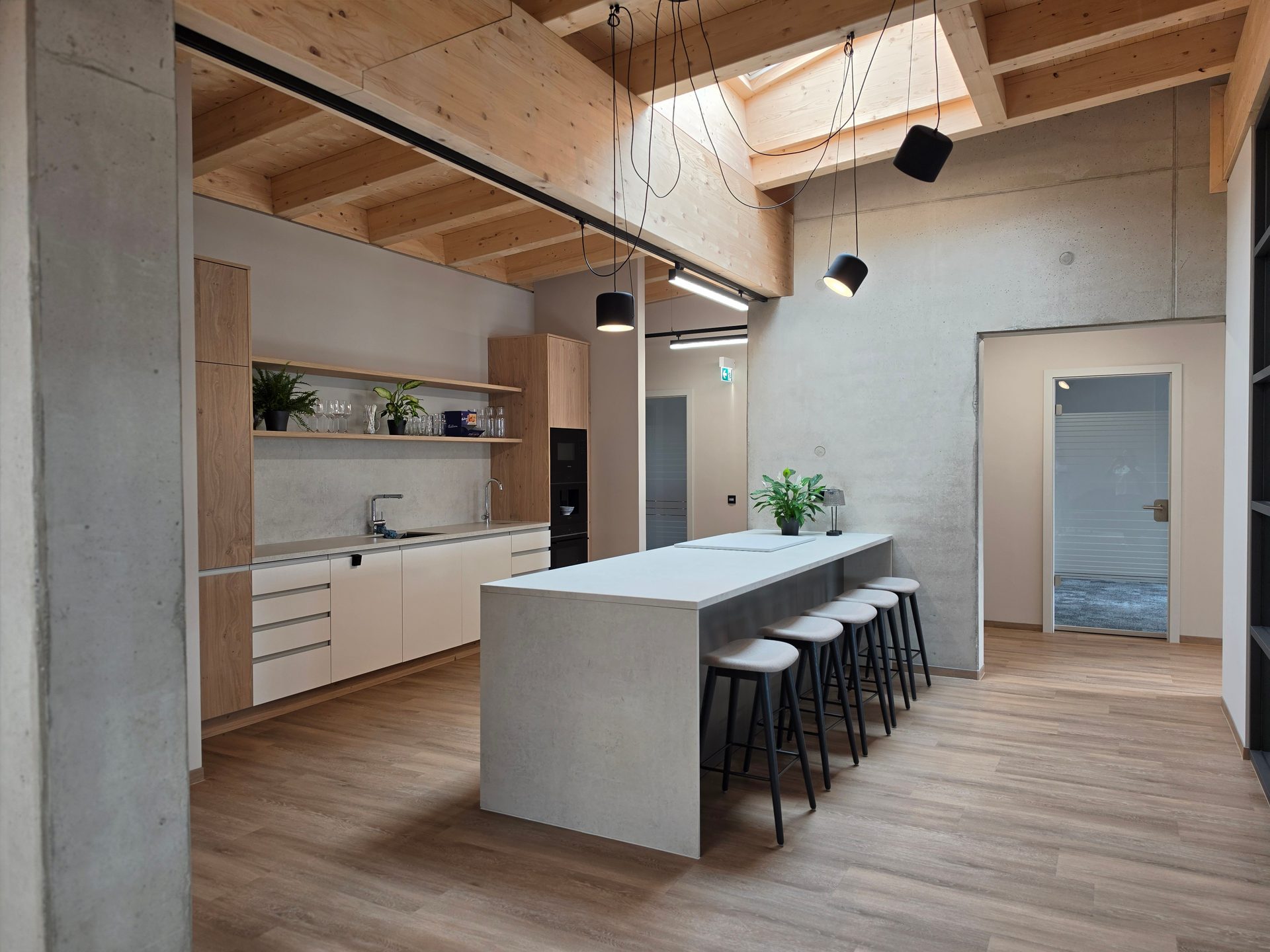 Modern office kitchen with wooden beams, skylight, island with bar stools, and light cabinetry.