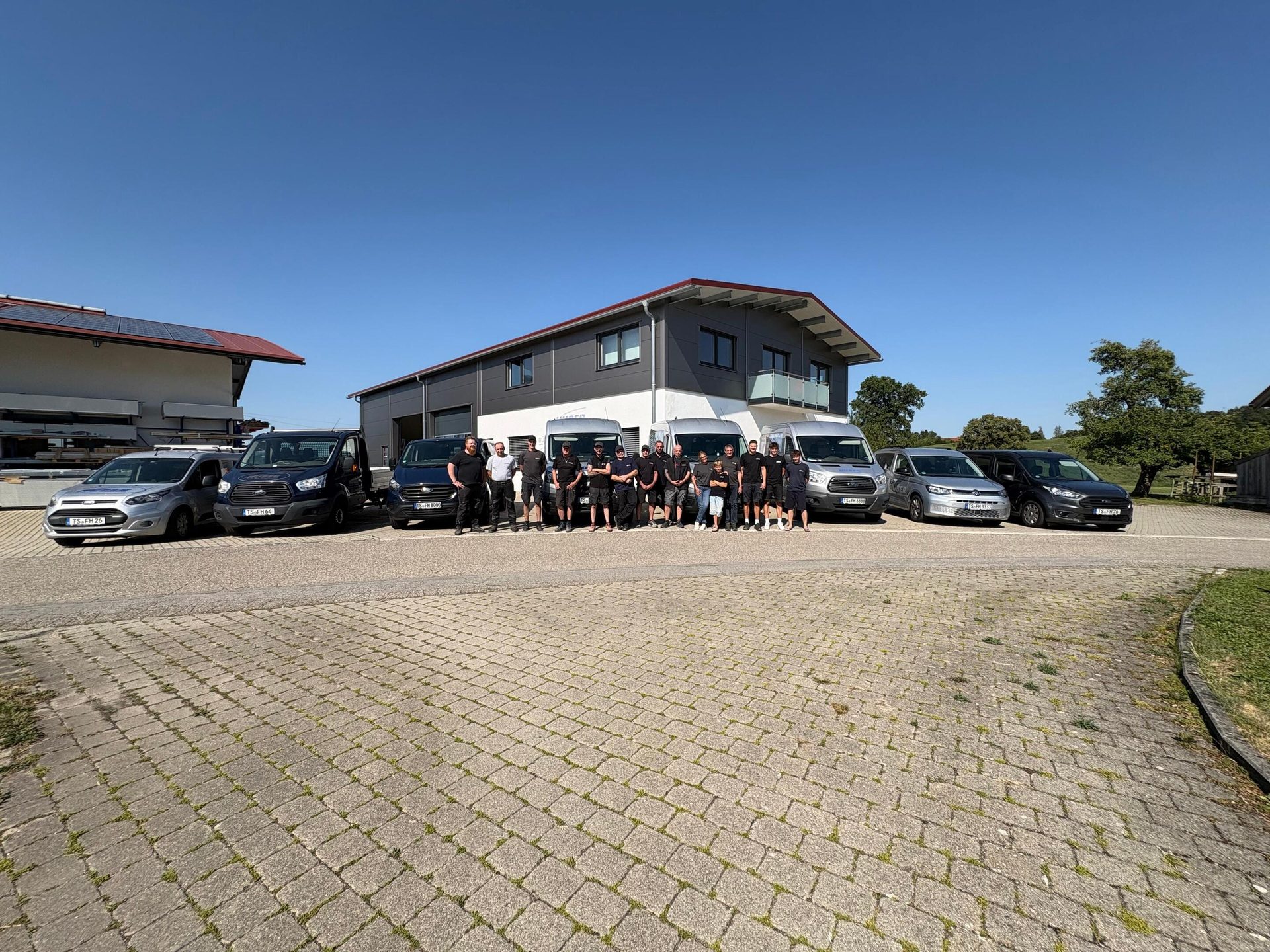A group of workers with their vans in front of buildings on a sunny day.