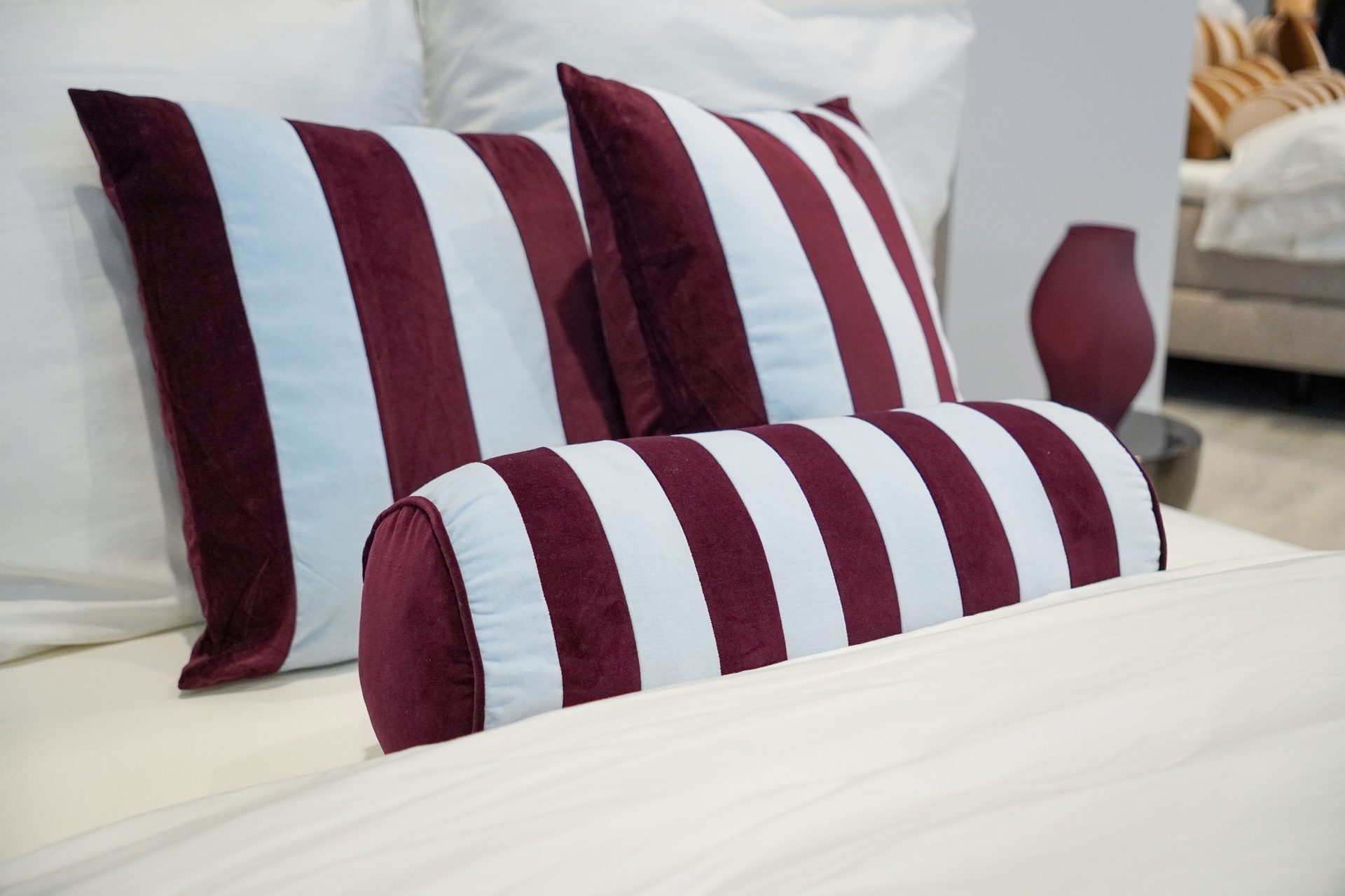 Burgundy and light blue striped velvet pillows and a bolster on a white bed.