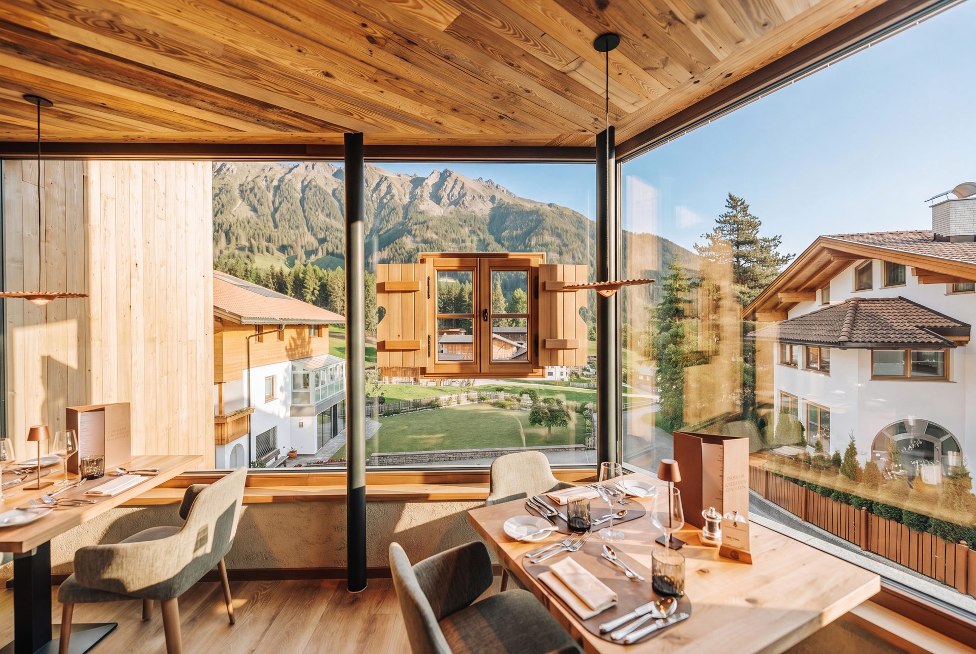 Modern restaurant interior with wooden ceiling and large windows offering panoramic mountain views.