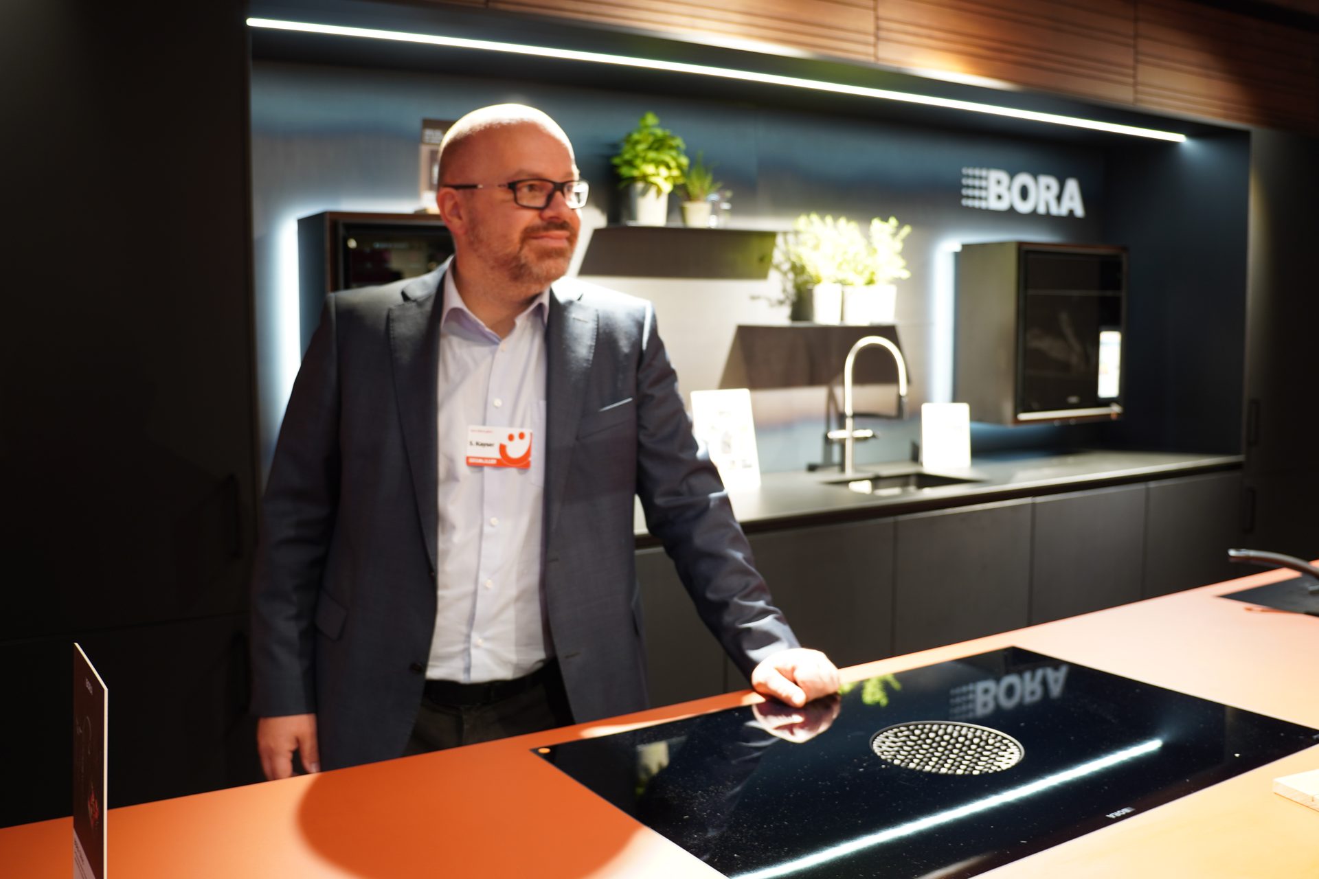 Man in a suit with a nametag showcasing a modern kitchen with a BORA induction cooktop.