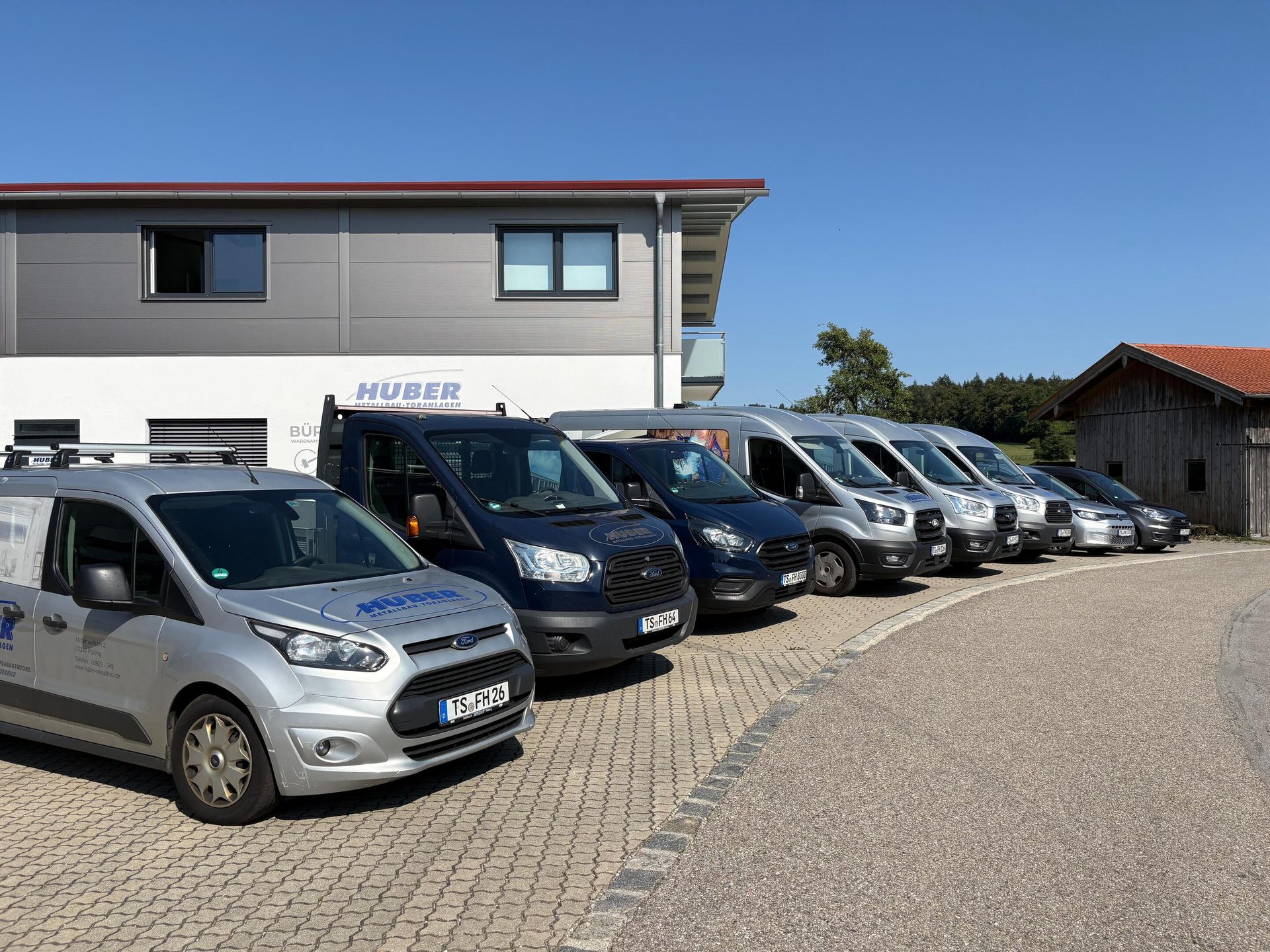 A line of Huber company vans parked on a paved lot in front of their building under a blue sky.