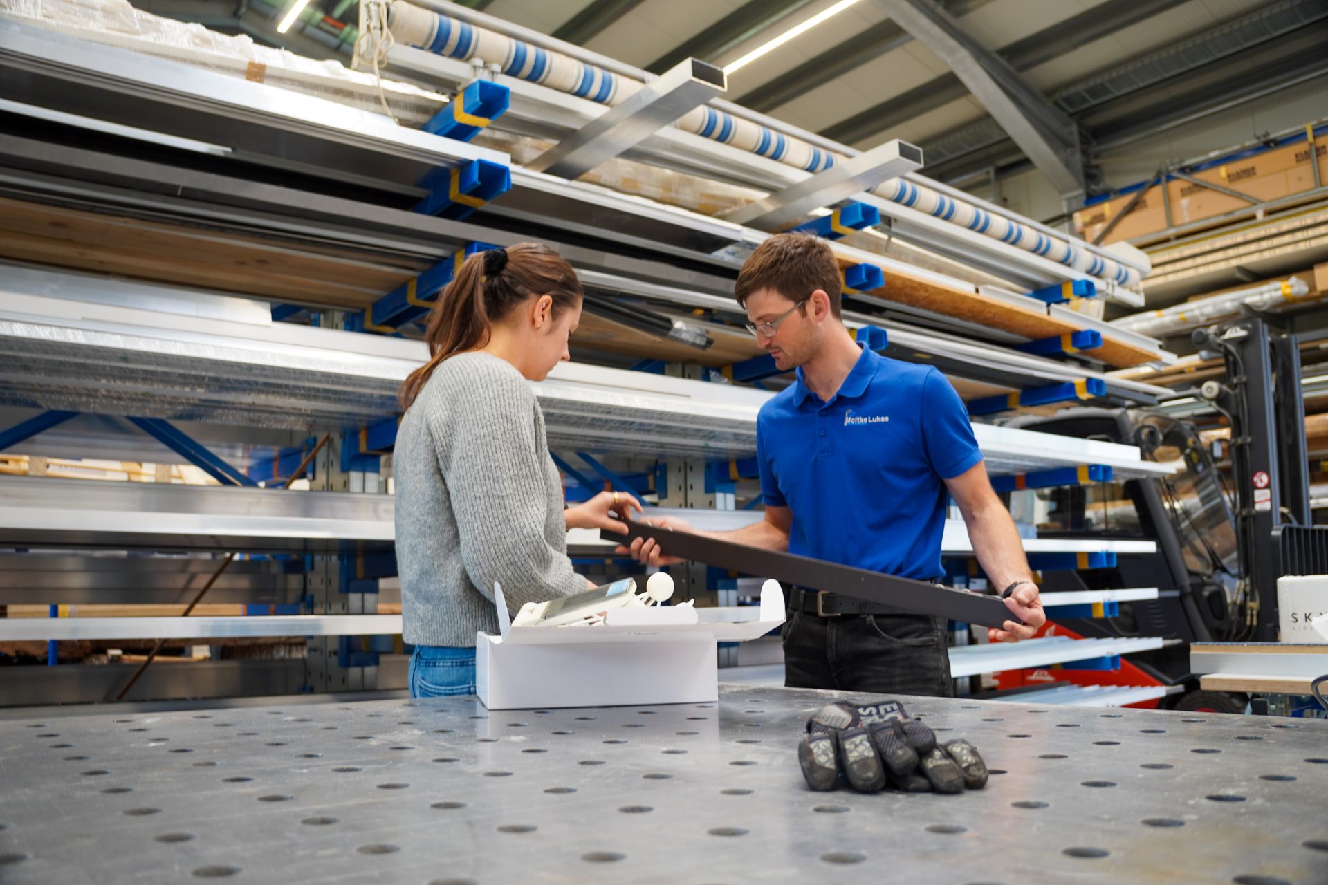 Two workers, a man and a woman, inspecting a dark component in a factory setting.