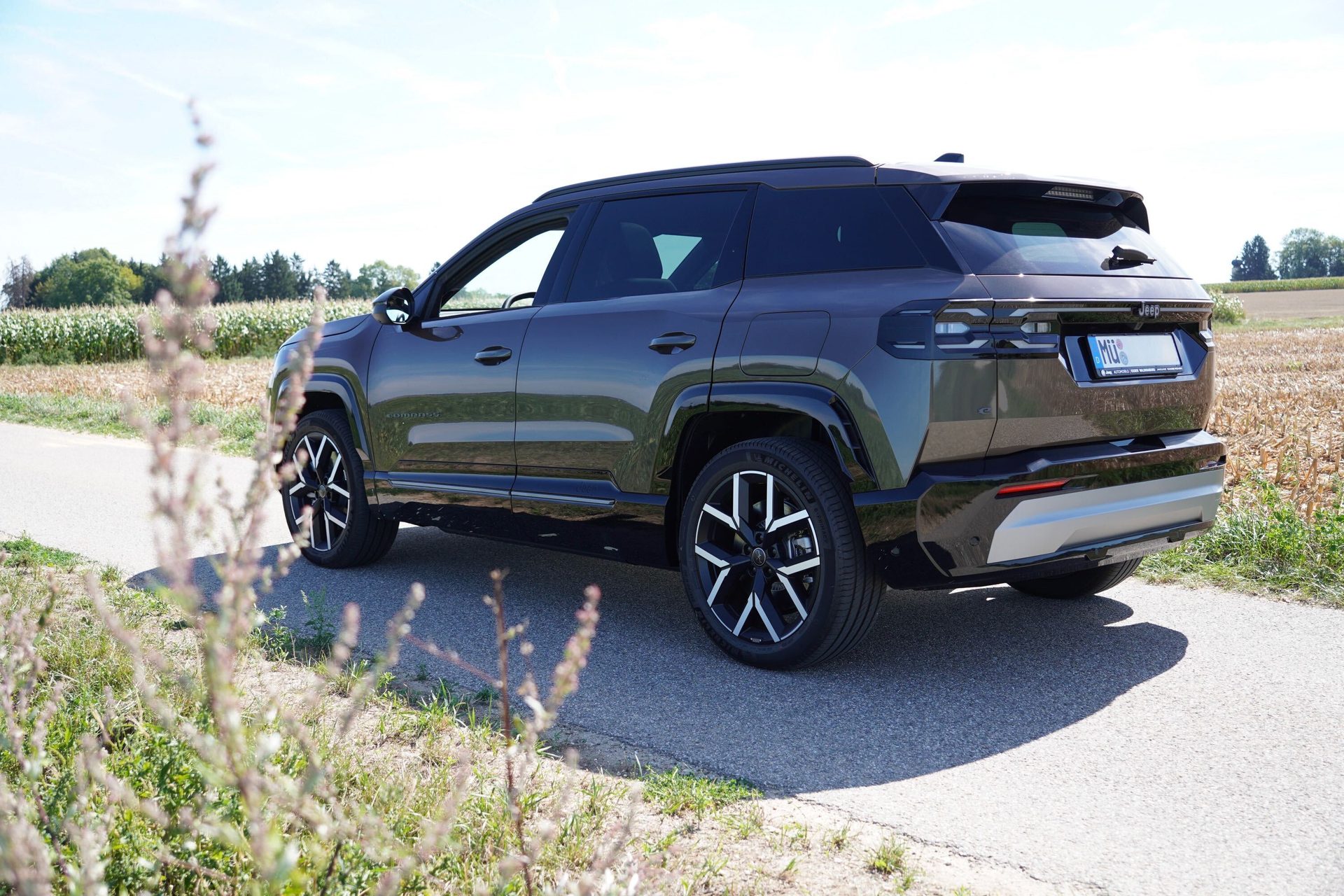 Dark grey SUV parked on a paved country road next to a dry field under a clear blue sky.