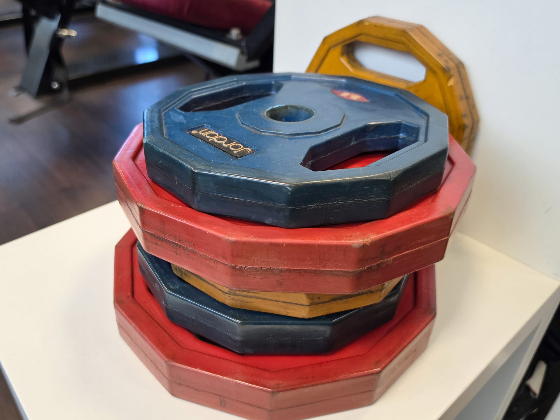 A stack of colorful, octagonal gym weight plates, including blue, red, and yellow, on a white surface.
