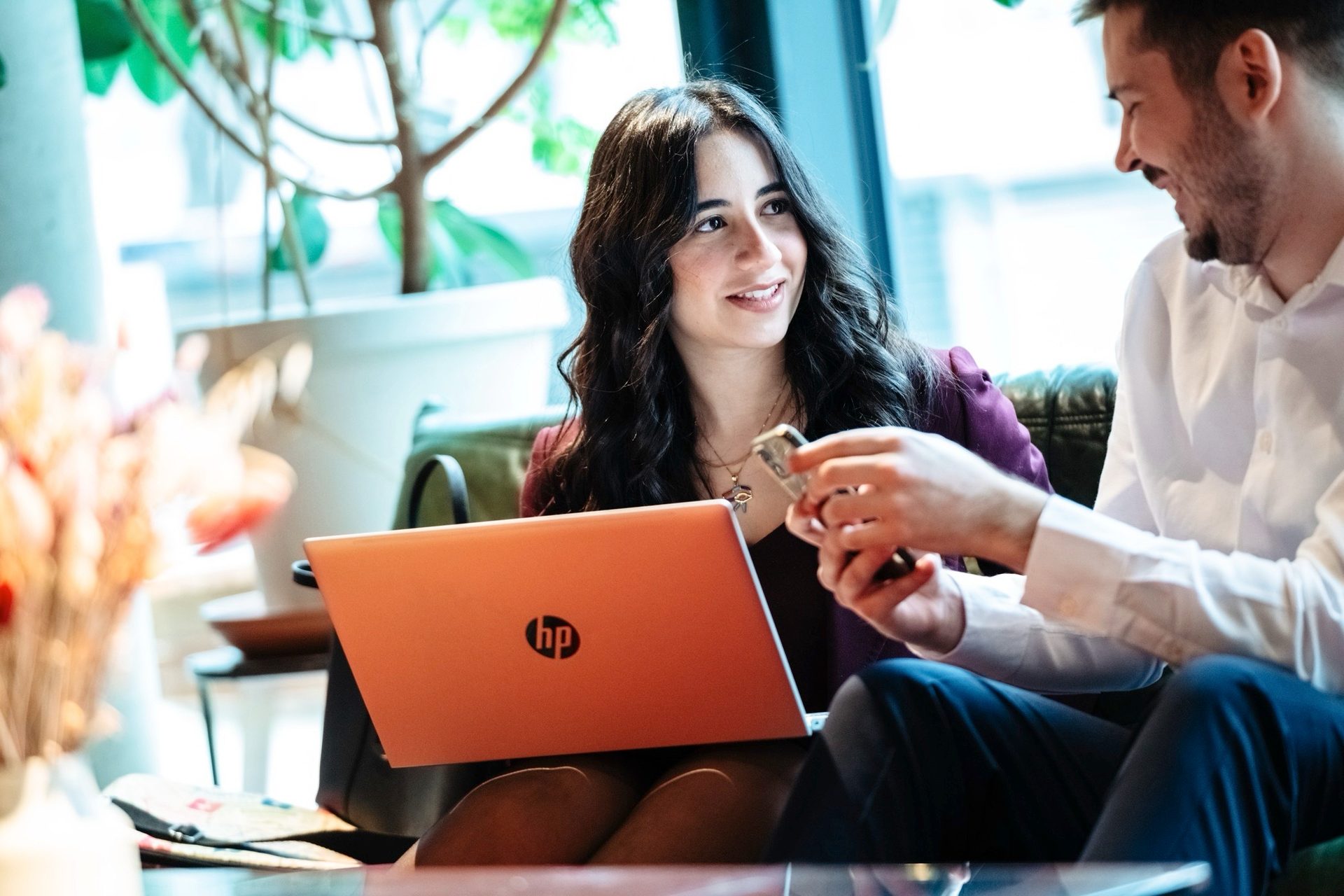 Smiling woman with orange HP laptop, man with phone, engaged in conversation.