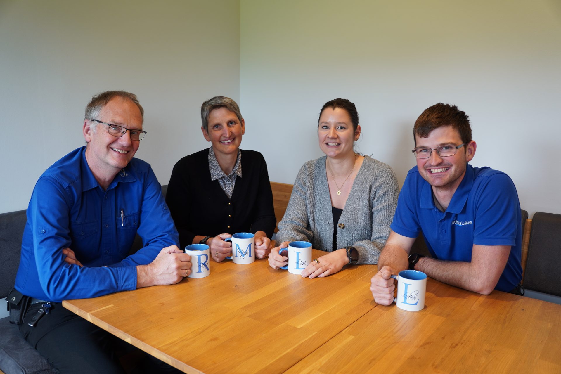 Four smiling colleagues, two men and two women, sitting around a table with personalized mugs.