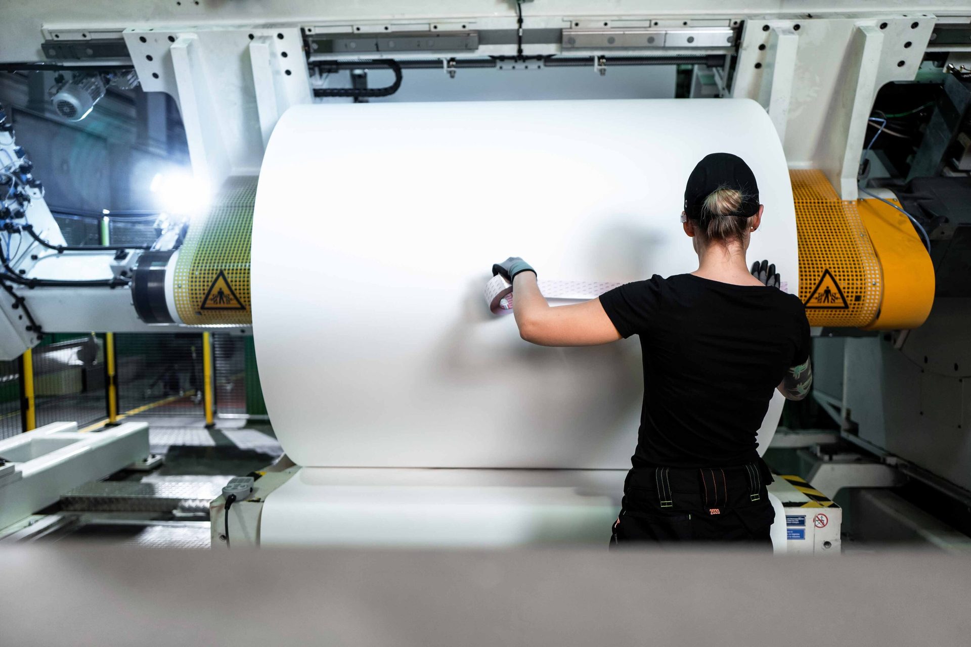 Worker taping a large white paper roll in a factory.