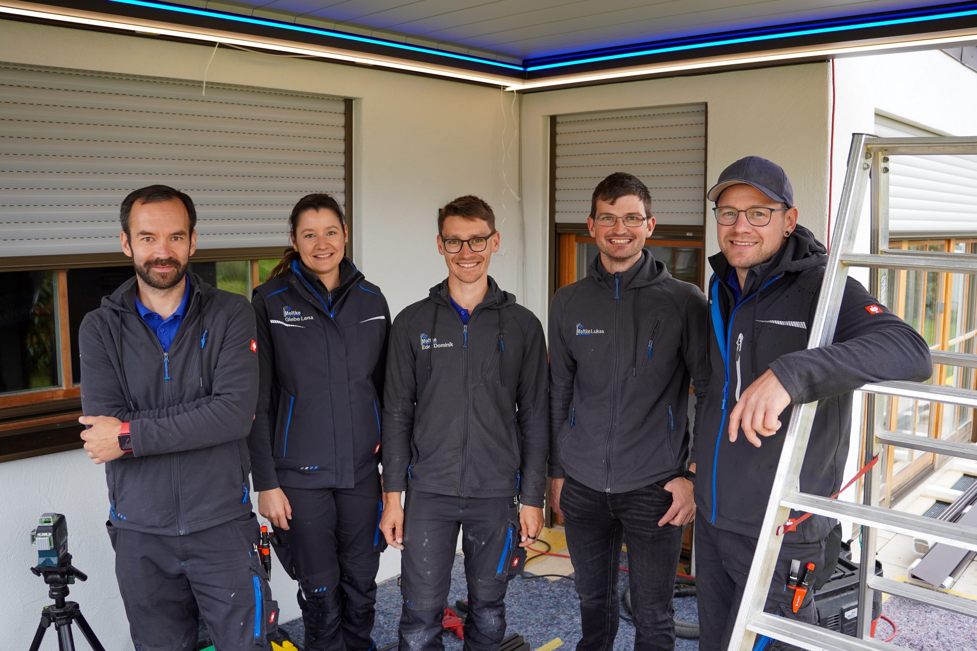 Five smiling construction workers, one woman and four men, in uniform, stand together.