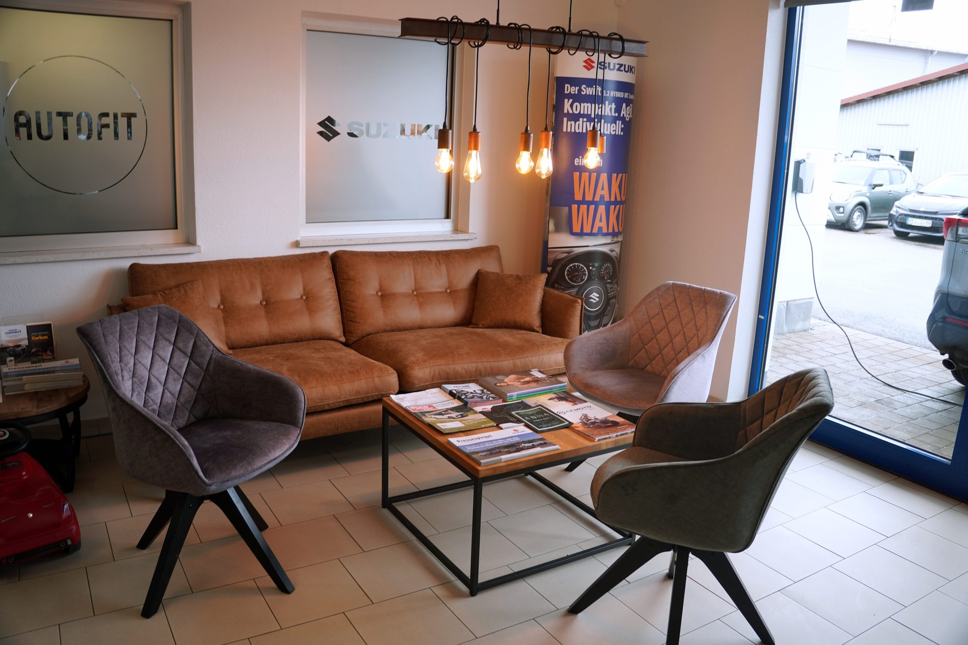 Cozy waiting area with a brown sofa, armchairs, coffee table with magazines, and industrial lighting.