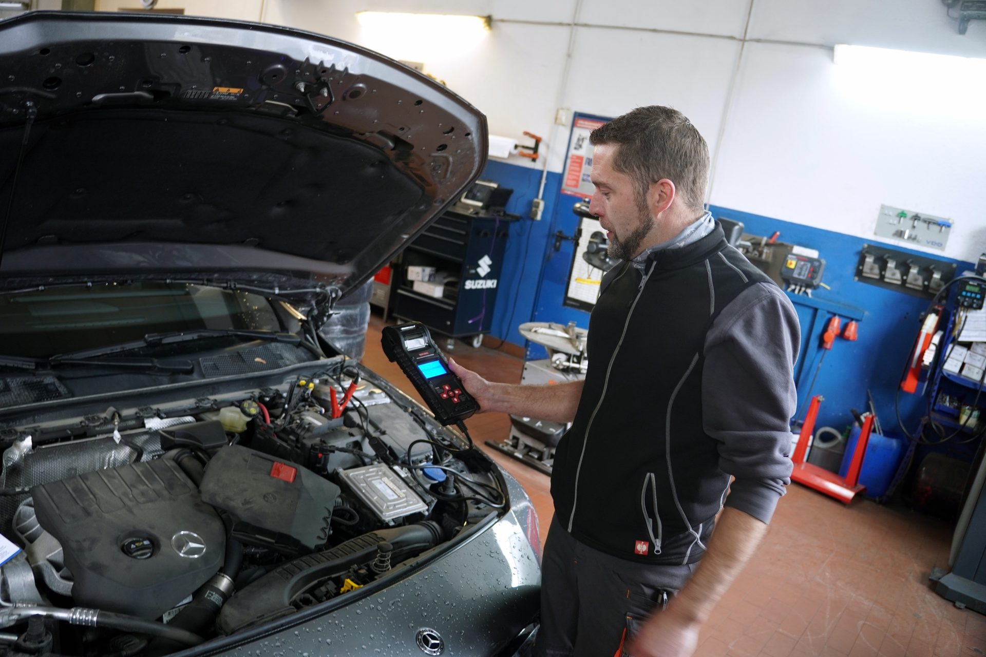 Mechanic uses a diagnostic tool to check a car engine in a garage, with the hood open for inspection.