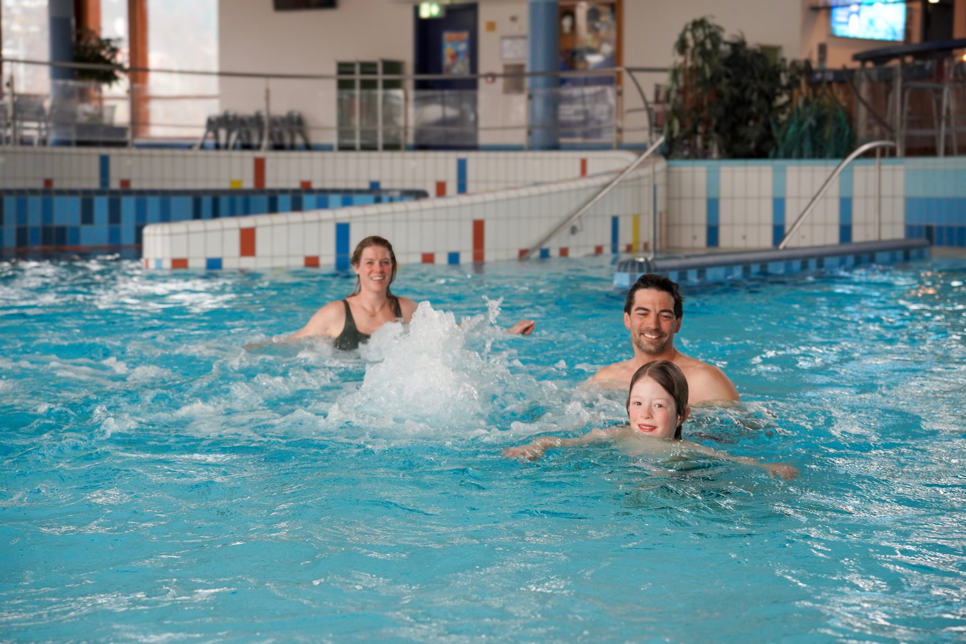 A family of three, including a woman, a man, and a child, smiling and enjoying themselves in a swimming pool with bubbling water.