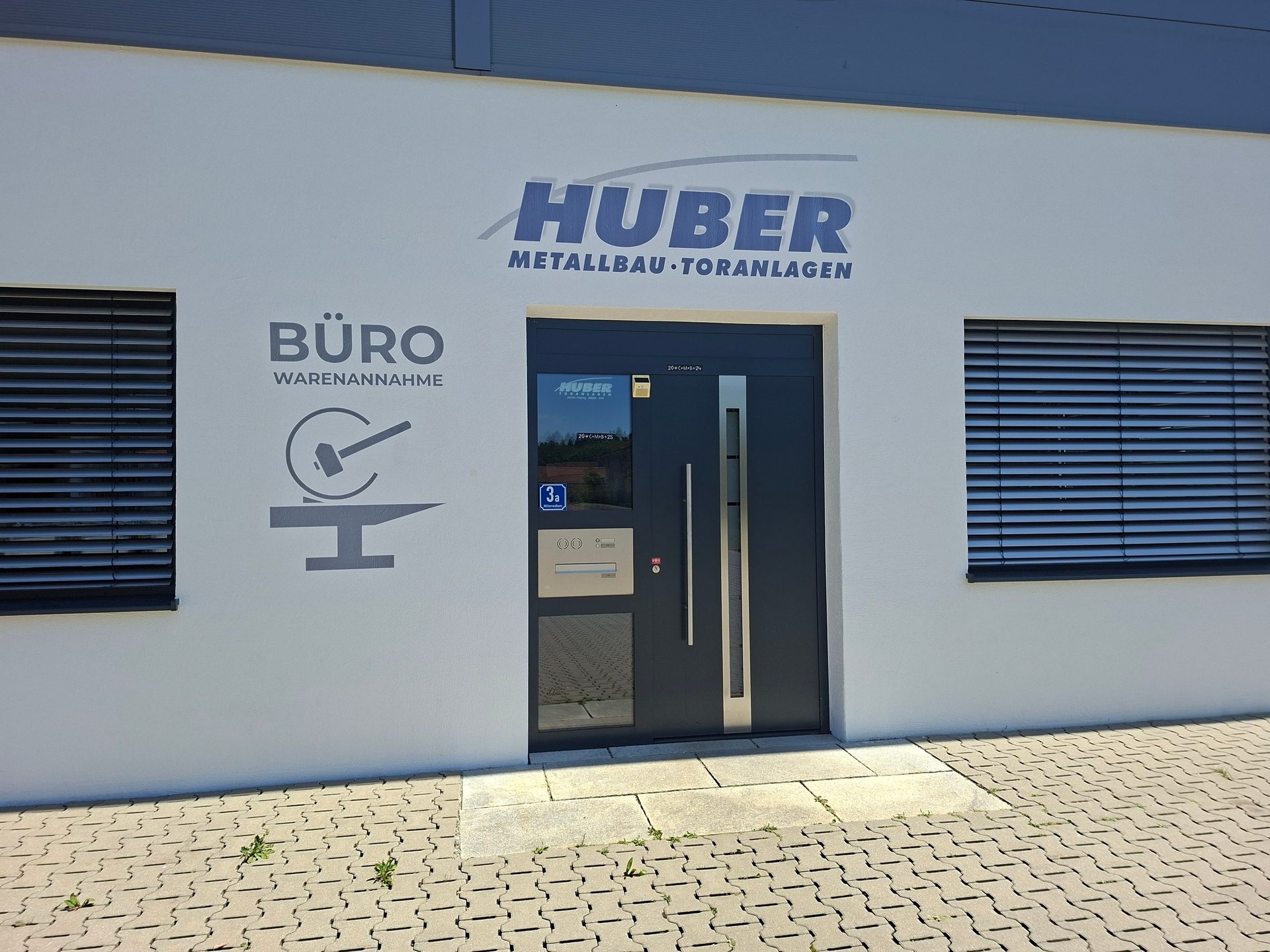 Huber Metallbau-Toranlagen building facade with "Büro Warenannahme" sign, entrance door, and windows.