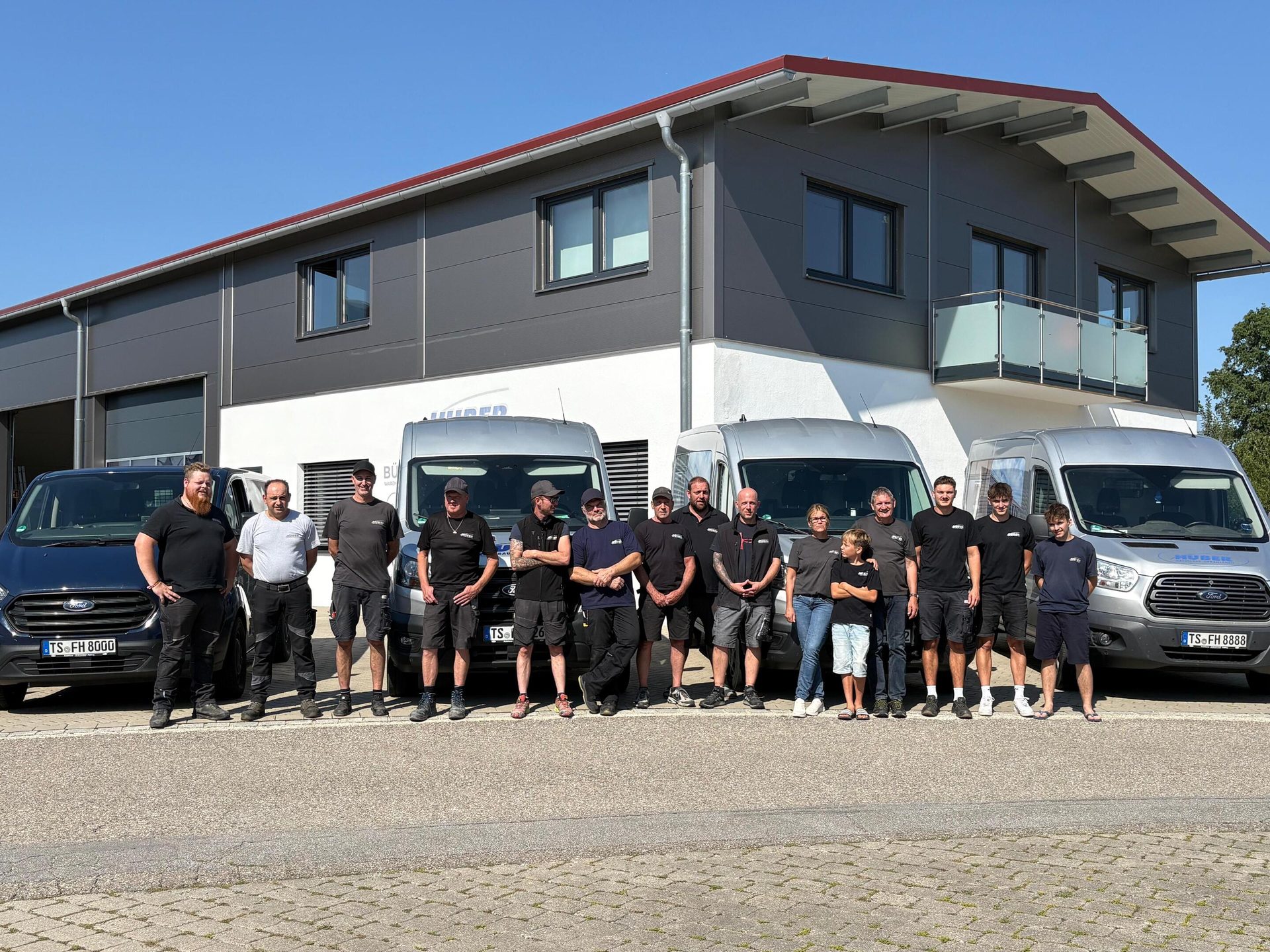 Team members and vans in front of a company building on a sunny day.