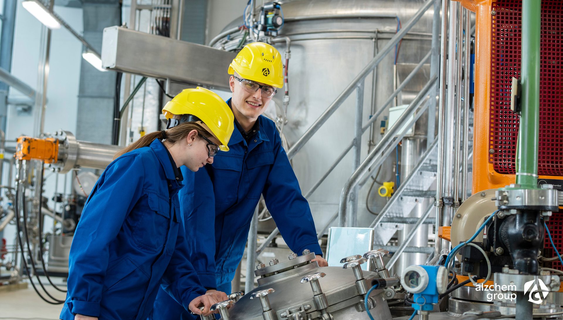 Workers in hard hats inspect factory equipment.